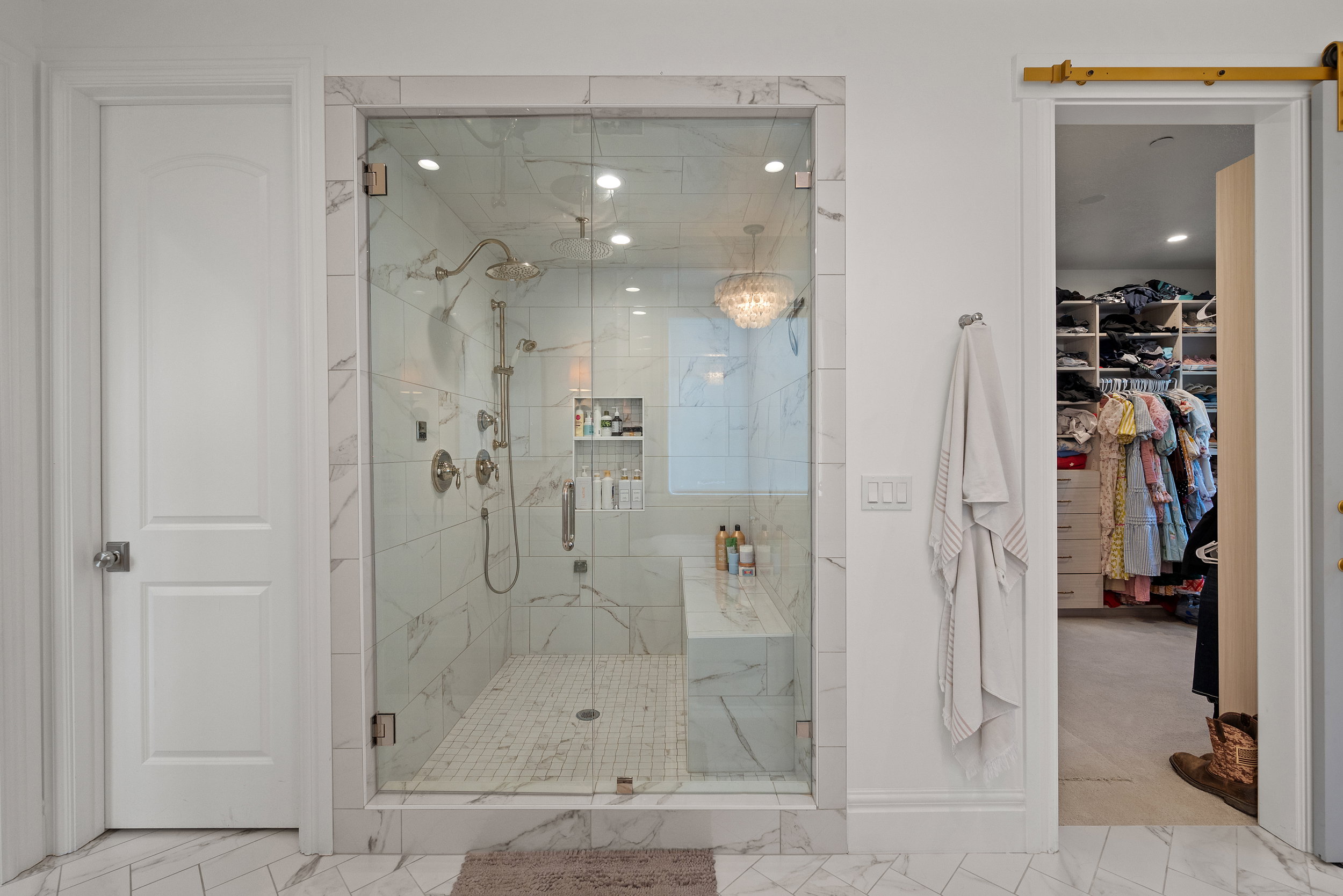 Glass-enclosed shower with a built-in bench and marble-style tile surround