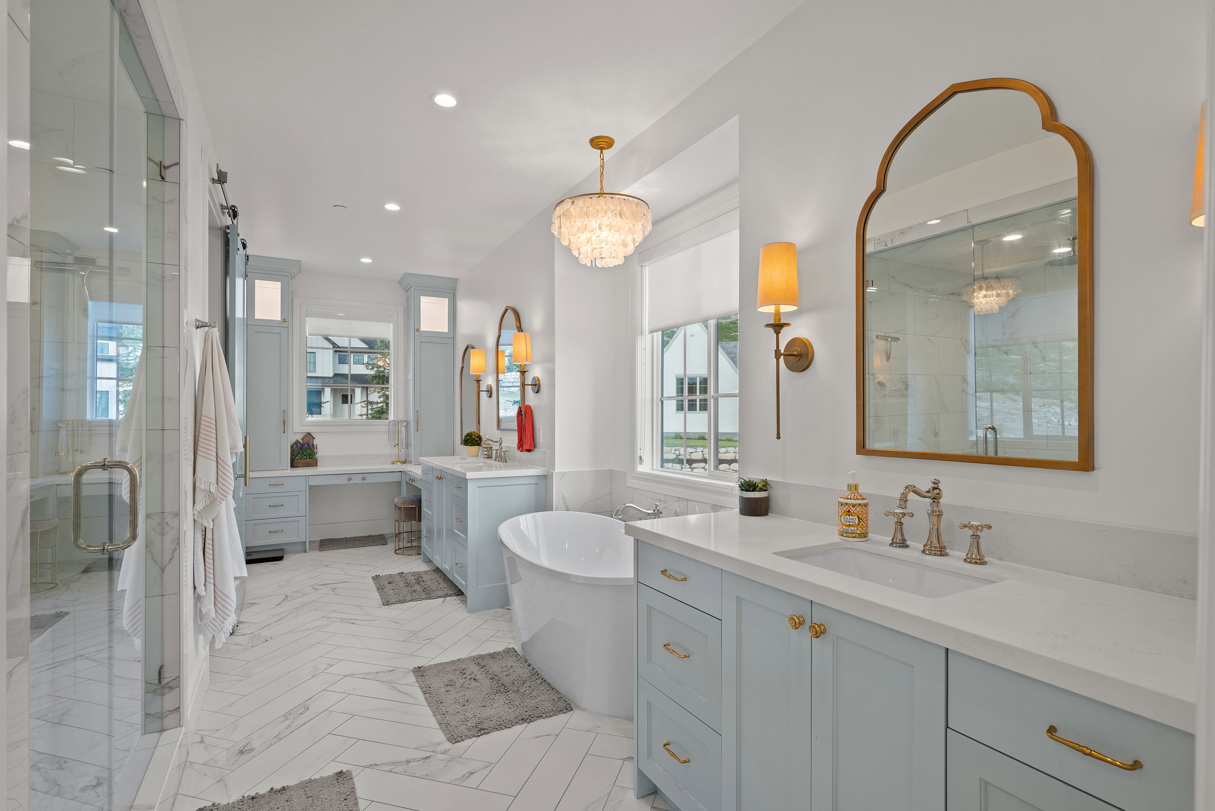 Spacious bathroom featuring a freestanding soaking tub, dual vanity with light blue cabinetry, a glass-enclosed shower, and herringbone pattern tile flooring
