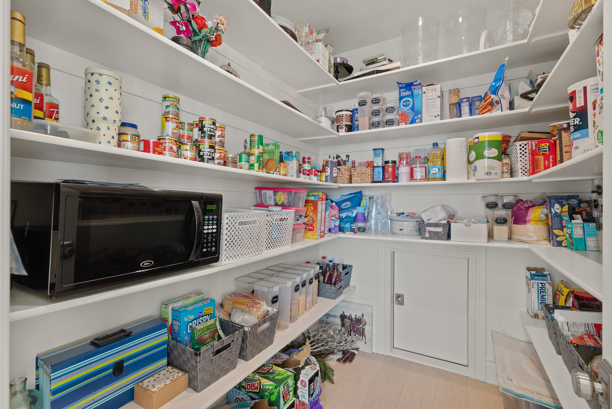 Pantry featuring extensive built-in shelving, white shiplap-style walls, light wood-finish flooring, and a built-in access panel