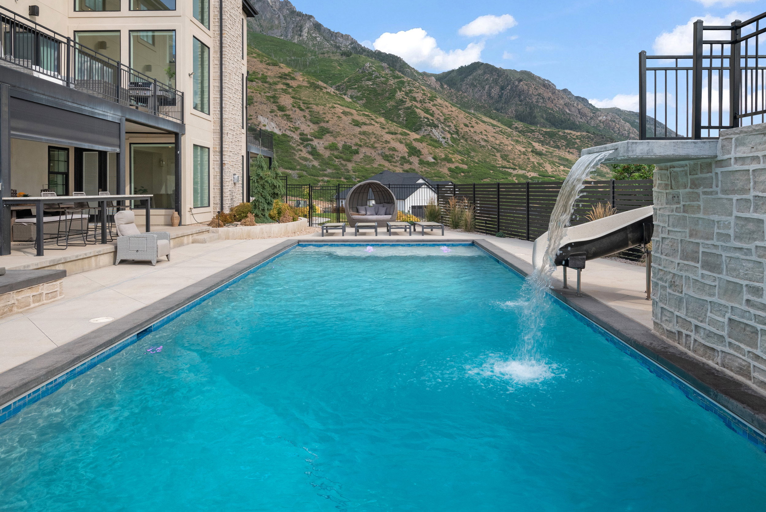 Expansive backyard featuring a rectangular swimming pool with a waterfall and slide, complemented by a large patio area with outdoor seating