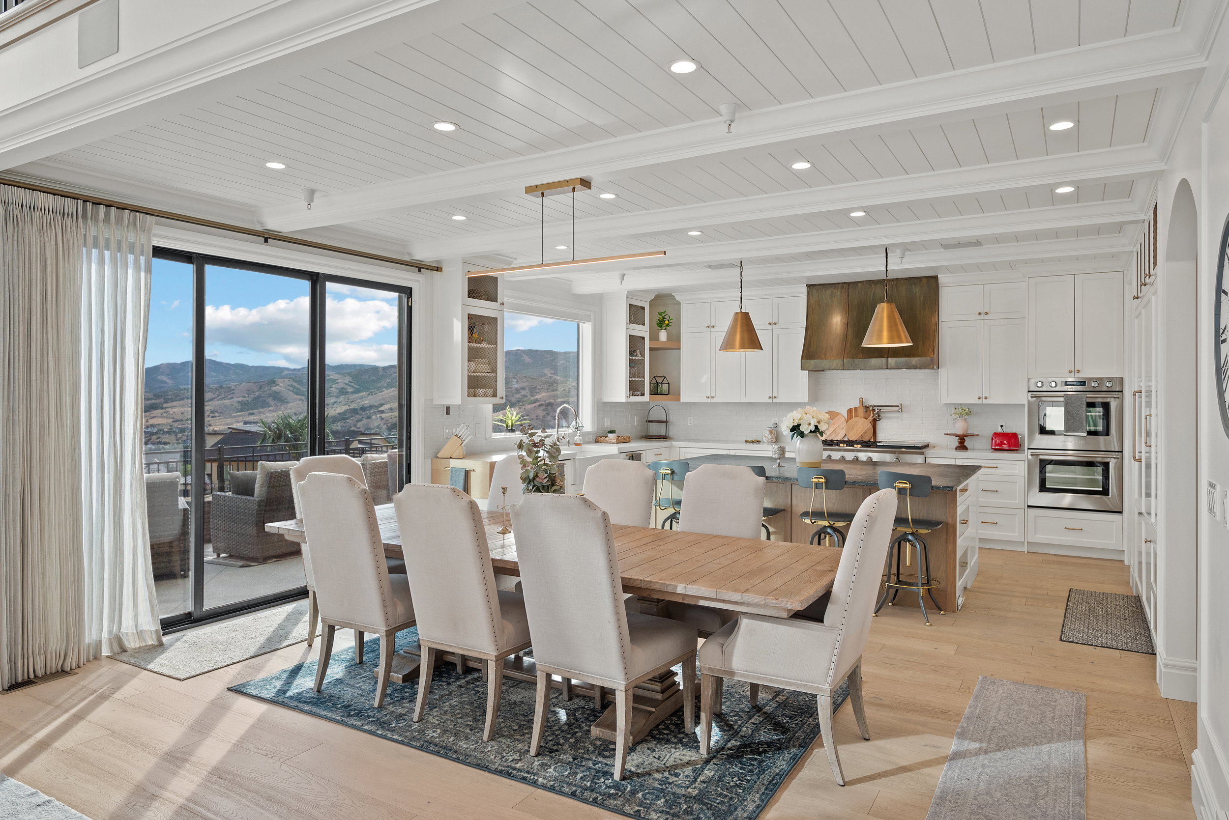 Open-concept kitchen and dining area featuring light wood-finish flooring, white shiplap ceilings with recessed lighting, and expansive glass sliding doors