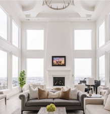 Spacious living area featuring a vaulted ceiling with a circular chandelier, a grand fireplace with a white mantel, and extensive windows showcasing distant scenery