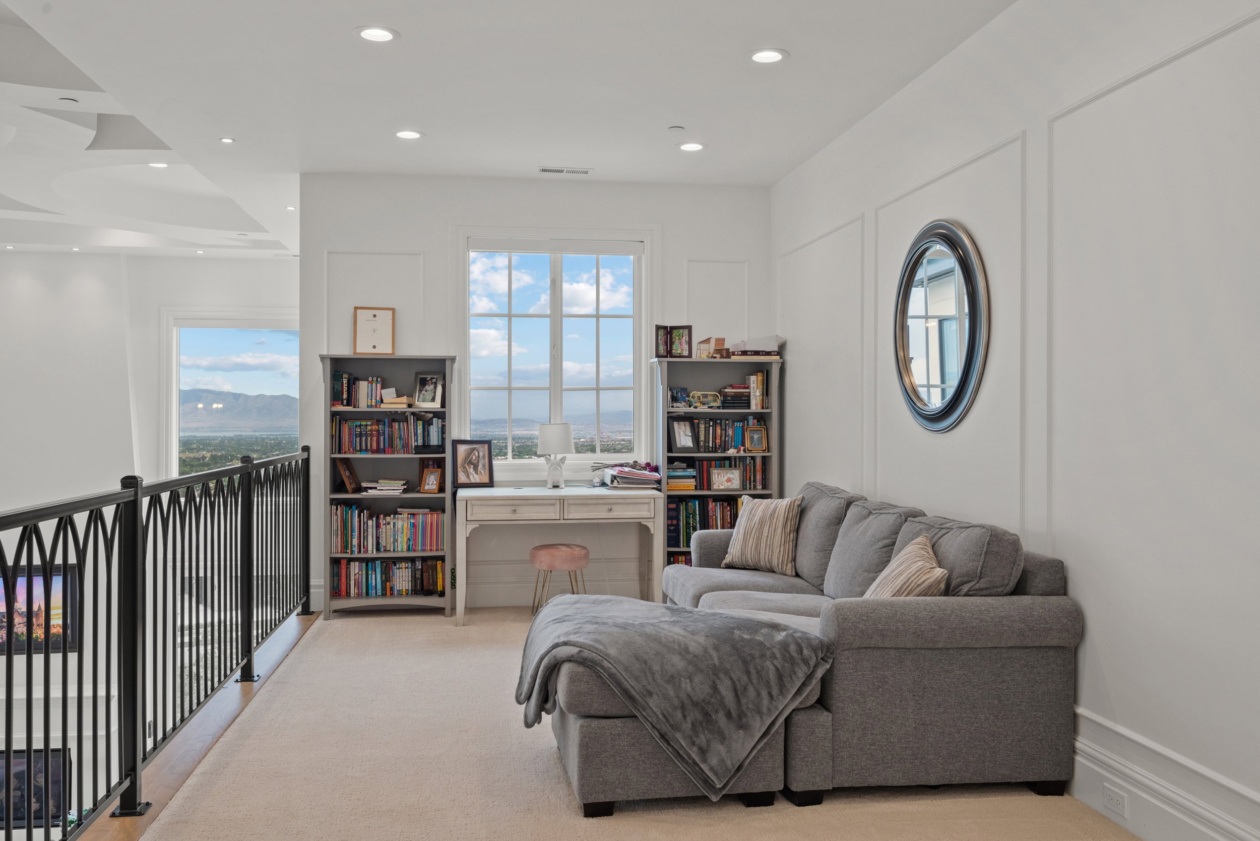 Loft space featuring a decorative black metal railing, window with distant mountainous scenery, recessed lighting, and wall panel molding
