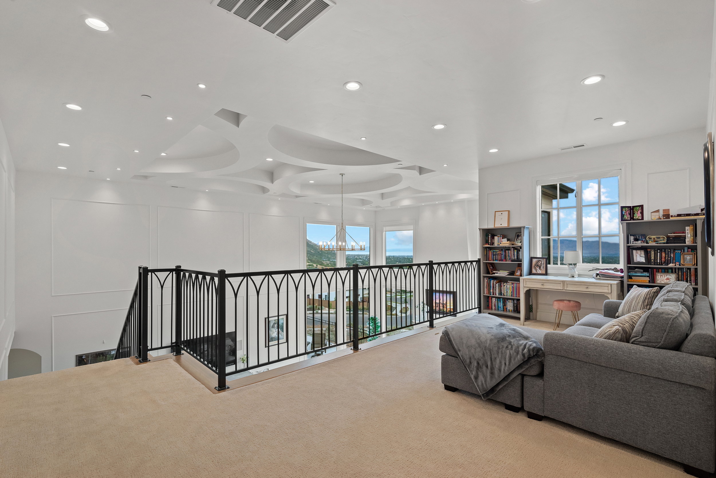 Loft space featuring a decorative ceiling design with recessed lighting, an ornate black metal railing, and large windows