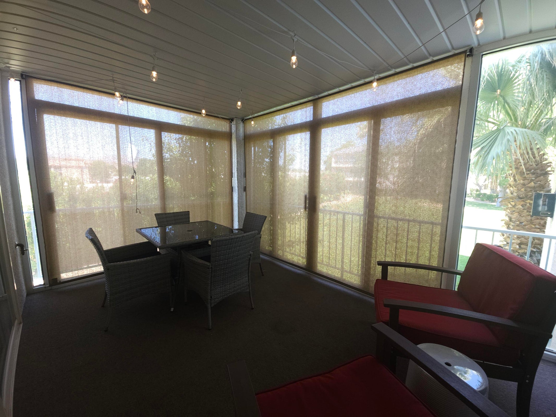 Enclosed patio featuring multiple sliding glass doors, neutral-toned roller shades, a slatted ceiling, and string lighting