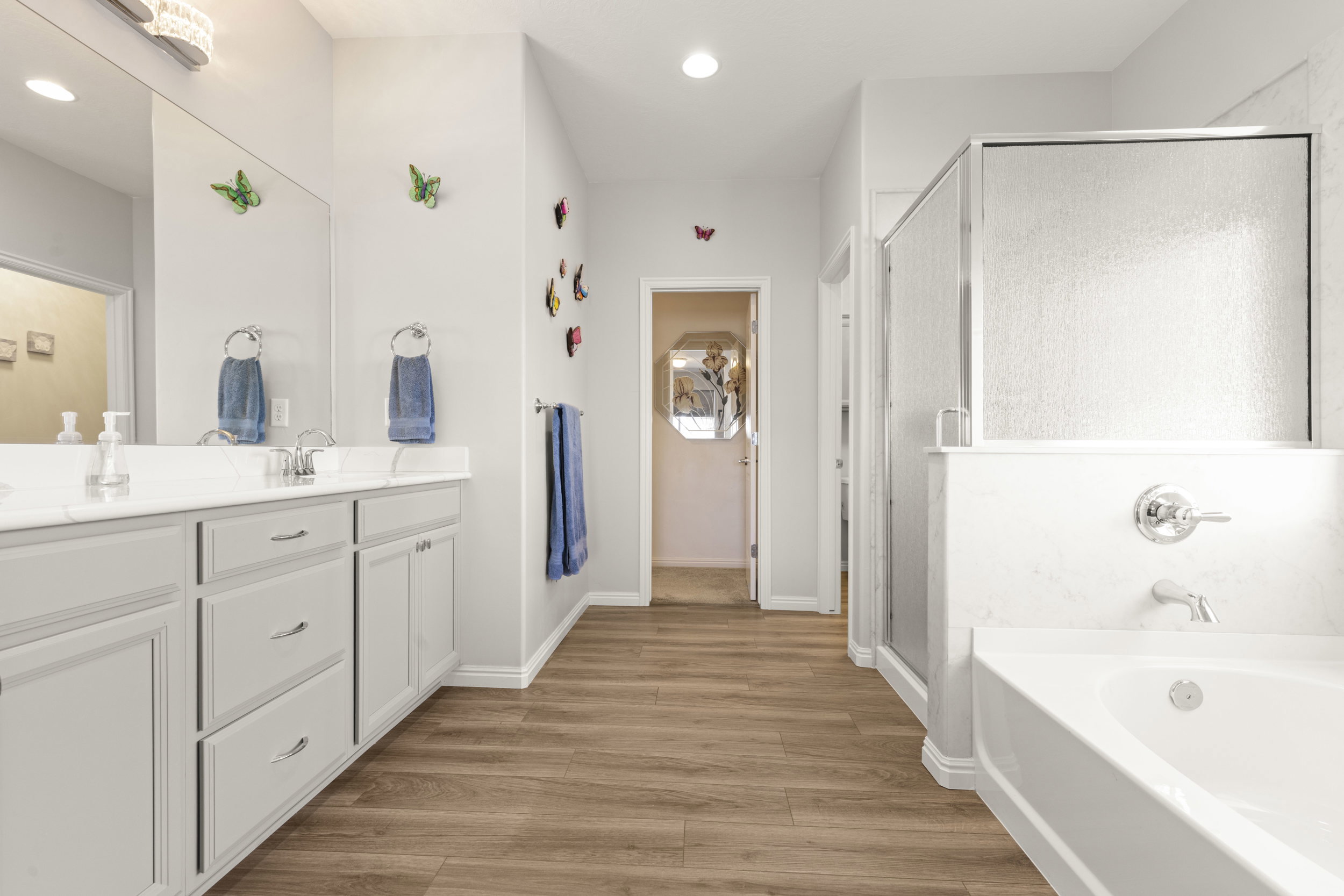 Bathroom featuring a double vanity with light-toned cabinetry, a built-in bathtub, and a separate shower enclosure with textured glass