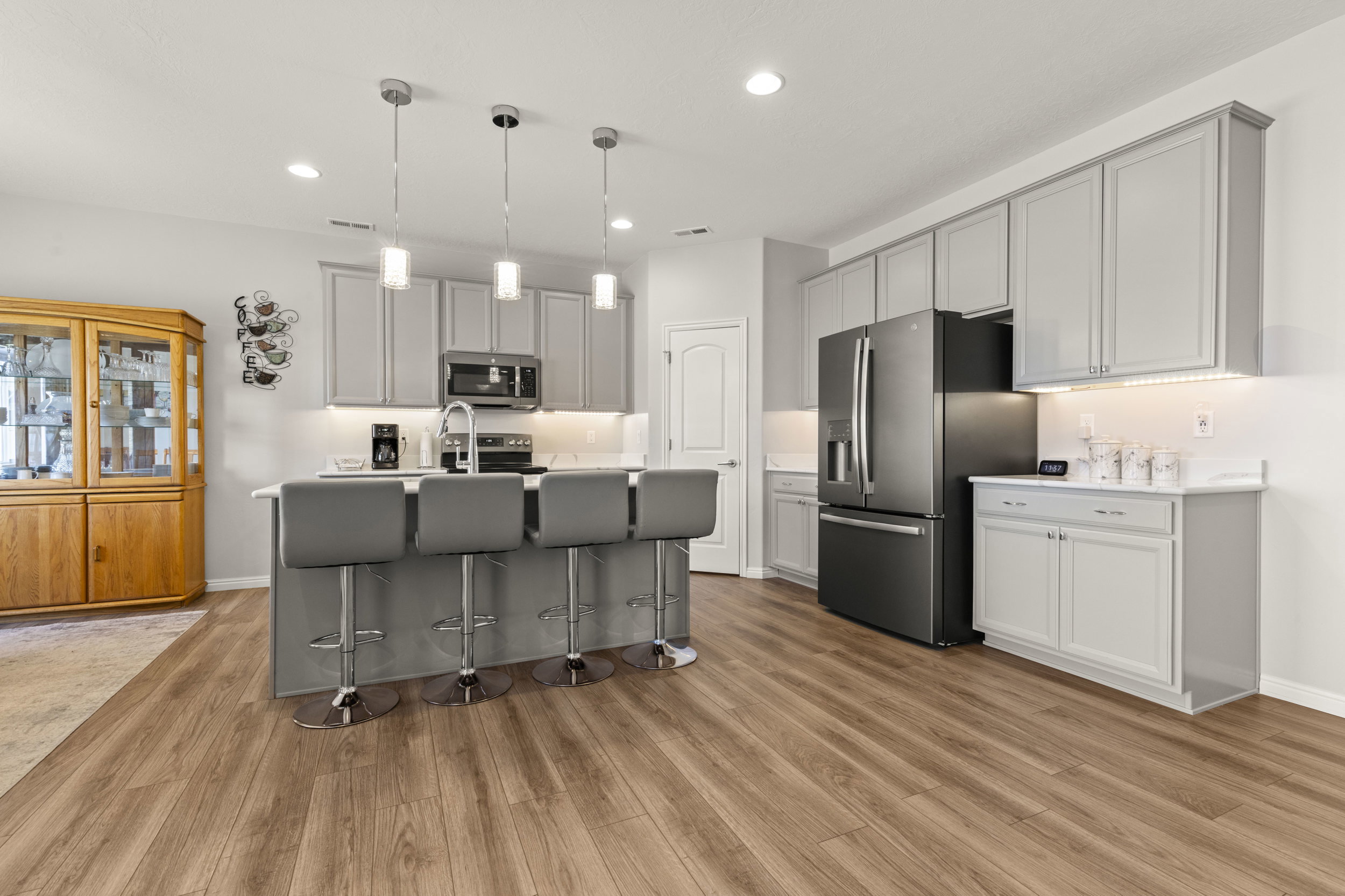 Contemporary kitchen featuring a center island with pendant lighting, stainless steel appliances, light gray cabinetry, under-cabinet lighting, and wood-finish flooring