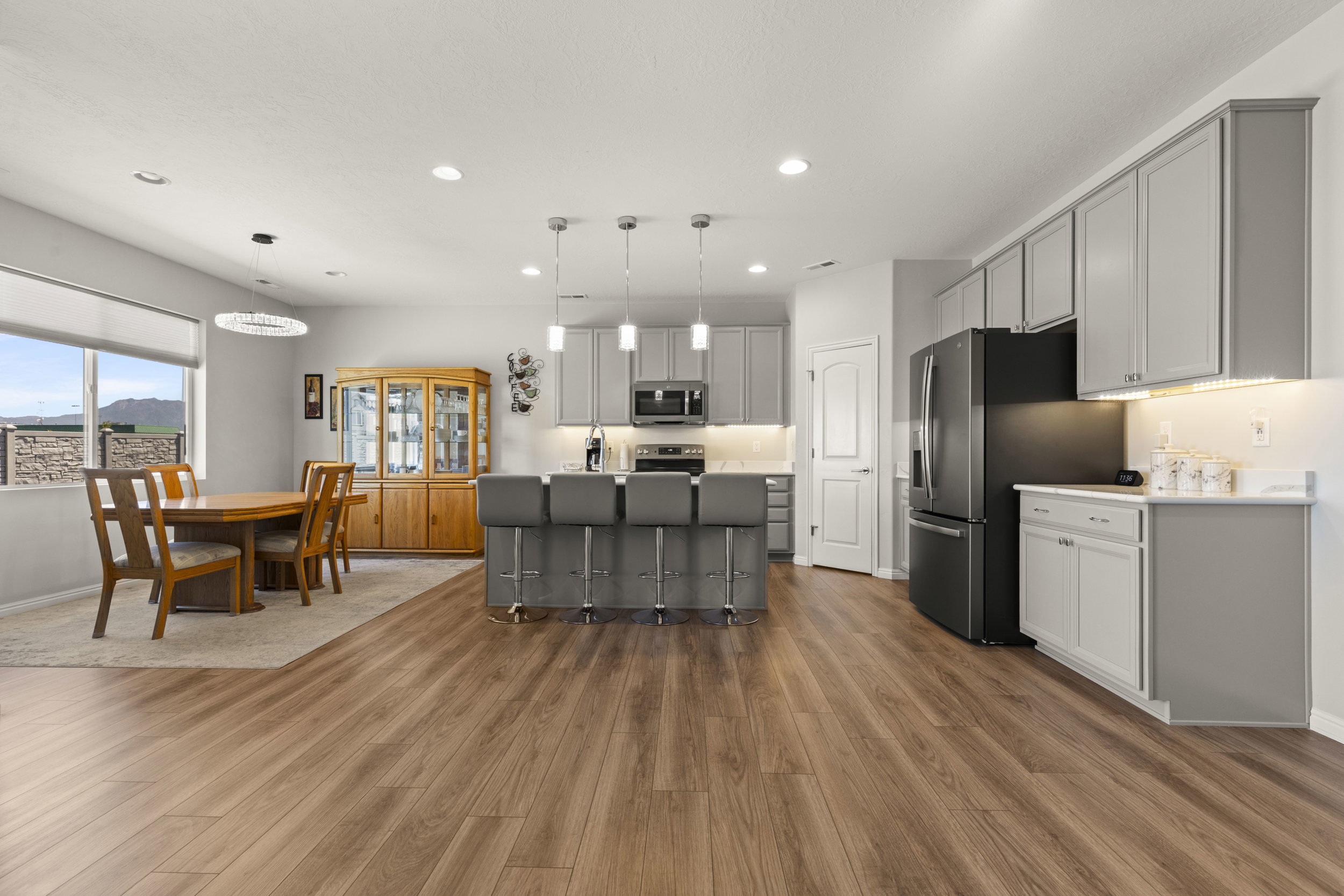 Open-concept living area featuring wood-finish flooring, a kitchen island with pendant lighting, gray cabinetry, black stainless steel appliances, and a dining area with a large window