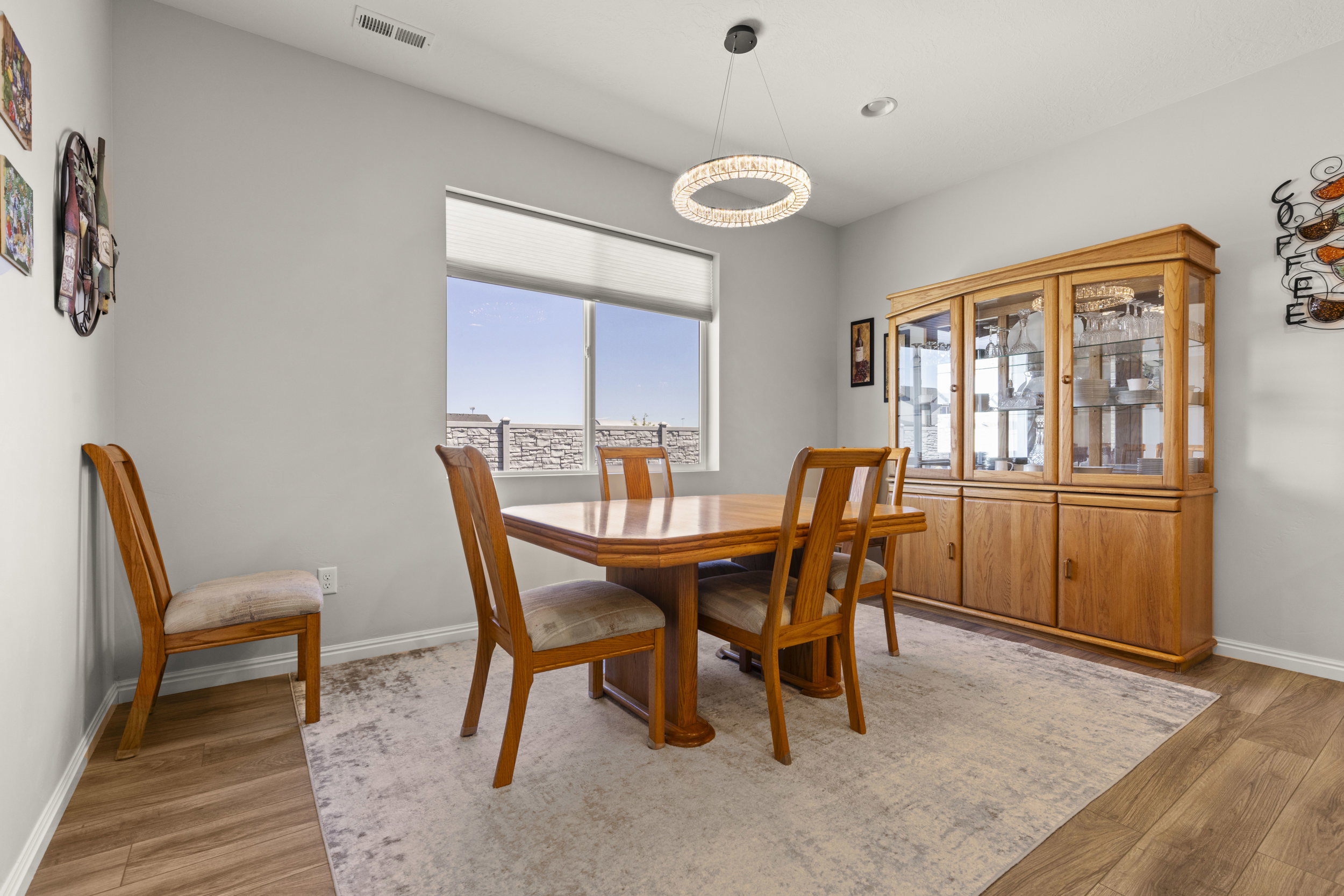 Bright interior space featuring wood-finish flooring, a contemporary chandelier, and a large window with roller shades
