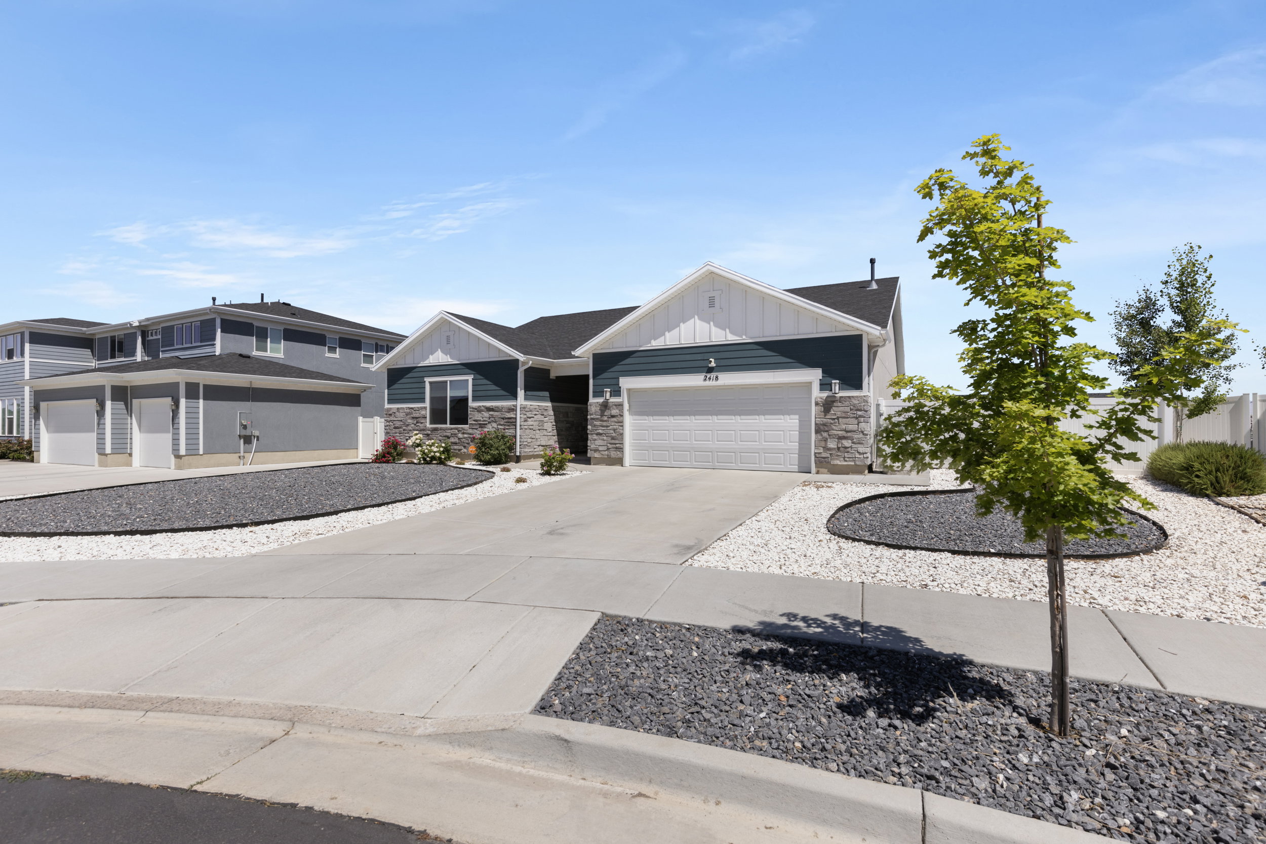 Single-story residence featuring a two-car garage, stone facade accents, dark grey siding, and white trim