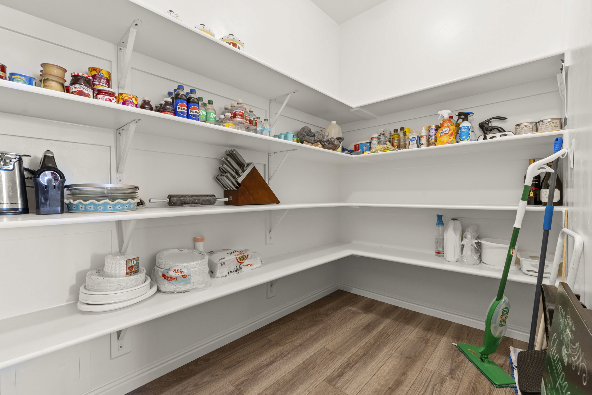 Walk-in pantry featuring extensive white shelving, white paneled walls, and wood-finish flooring