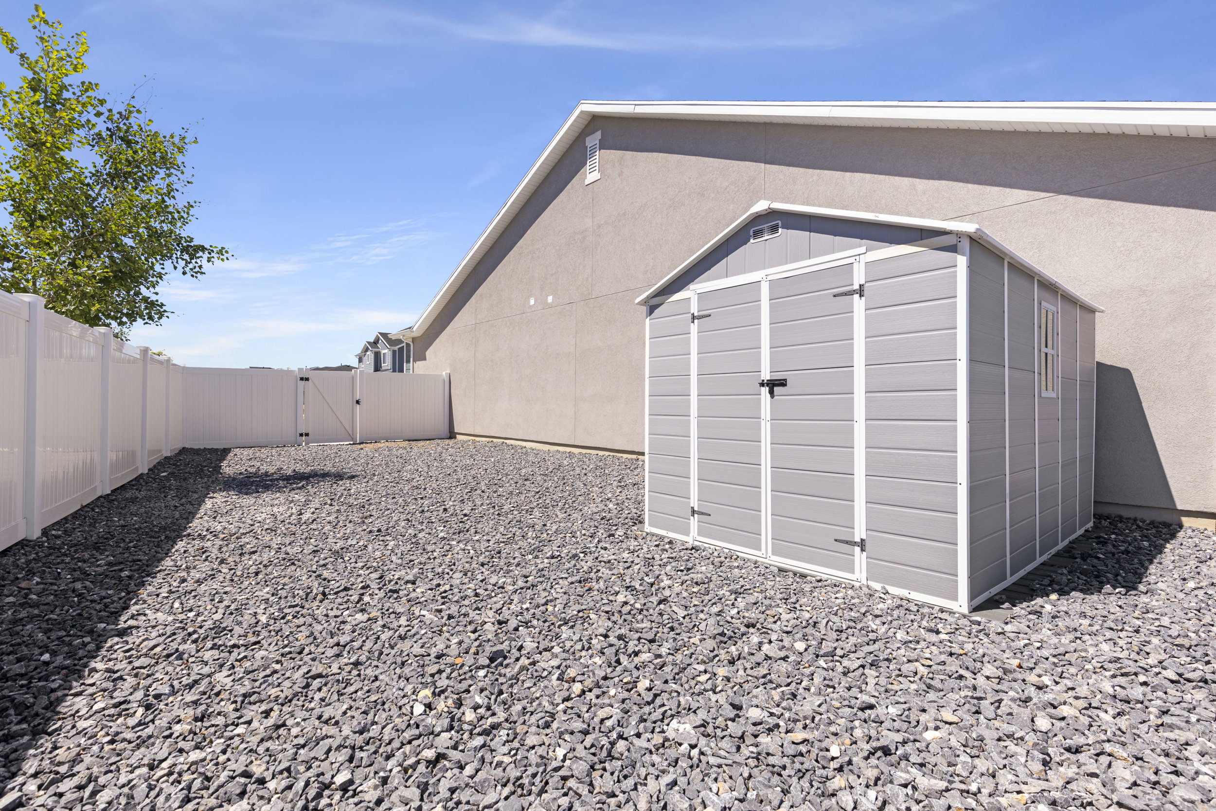 Gray utility shed with a gable roof, double doors, and a side window, situated on a gravel surface