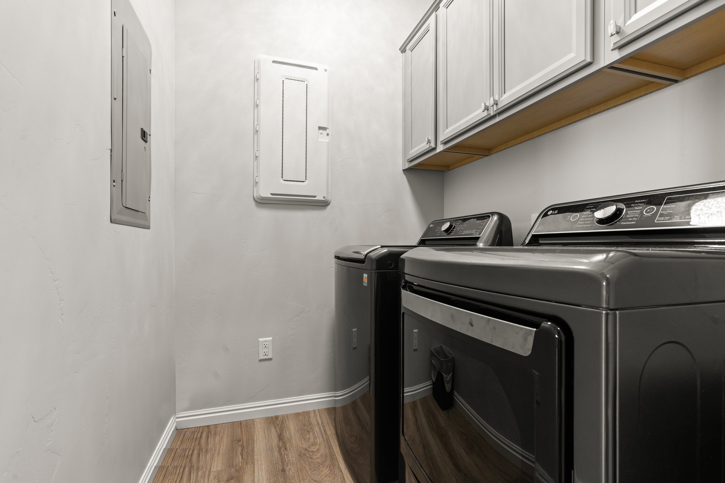 Utility room featuring wood-finish flooring, white baseboards, and overhead cabinetry