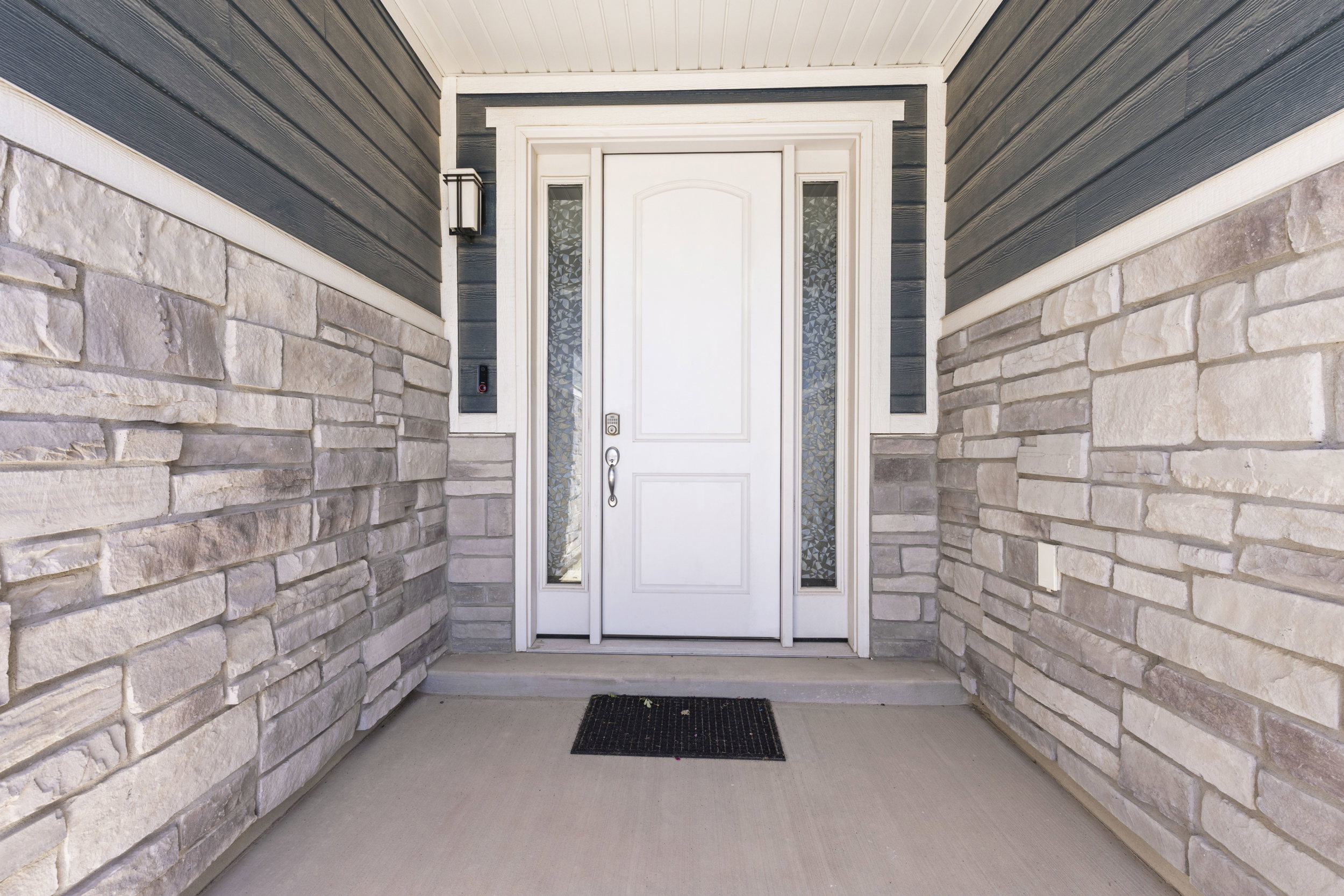 Inviting entryway featuring a white paneled door with decorative sidelights, complemented by an overhead light fixture