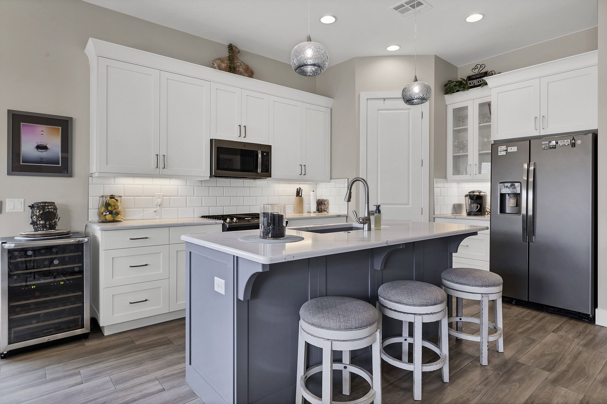 Modern kitchen featuring white shaker cabinetry, stainless steel appliances, a white subway tile backsplash, and a central island with a contrasting base and integrated sink