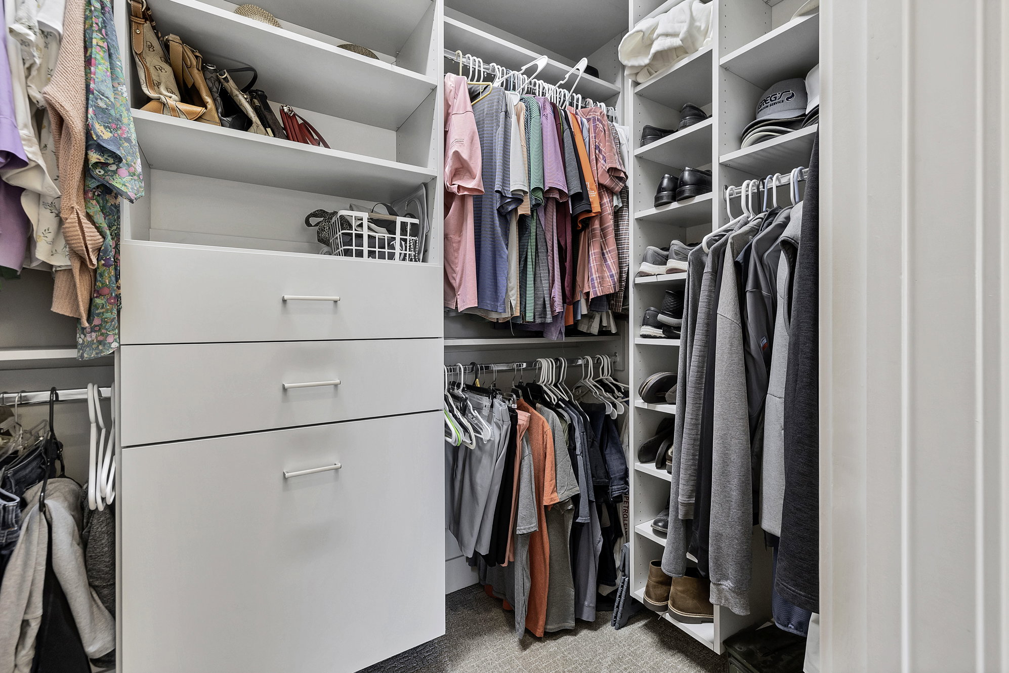 Custom closet system featuring white shelving, multiple hanging rods, integrated drawers with horizontal hardware, and dedicated shoe storage