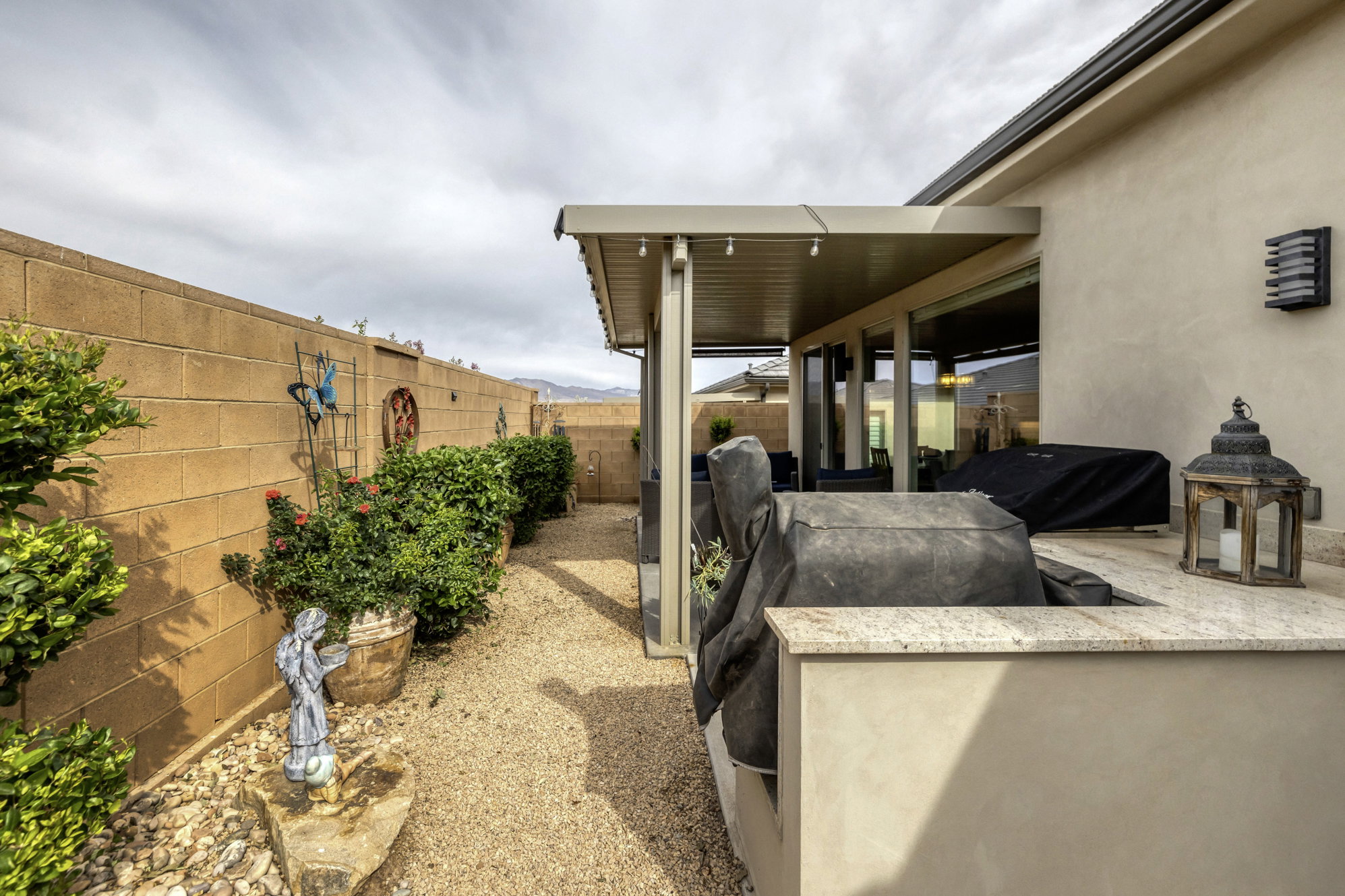 Outdoor kitchen with light-toned countertop, covered patio structure, and exterior wall lighting