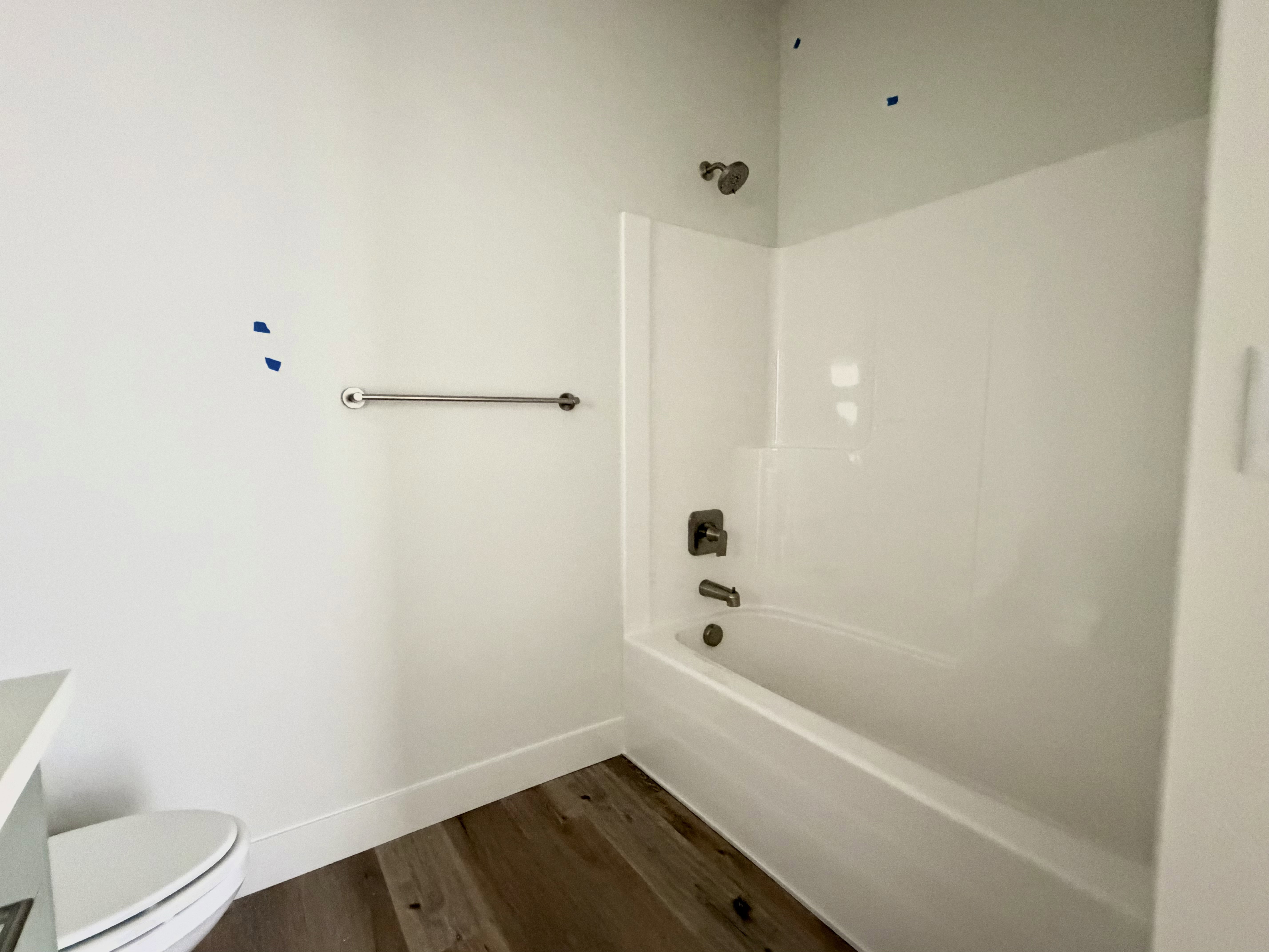 Bright bathroom featuring a white tub-shower combination, brushed nickel fixtures, and wood-finish flooring