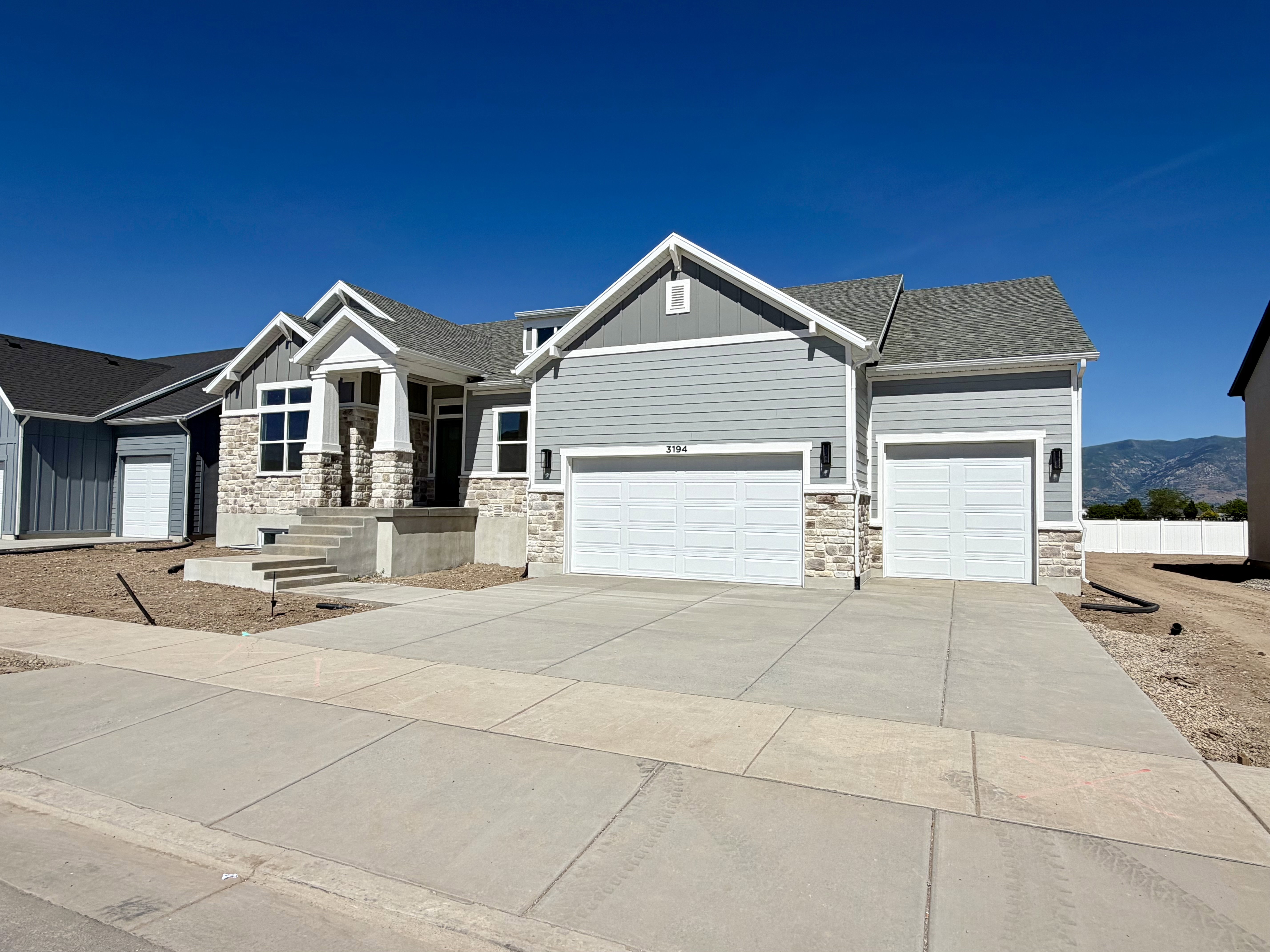 Contemporary exterior featuring light grey siding, stone accents, multiple gables, and a two-car garage