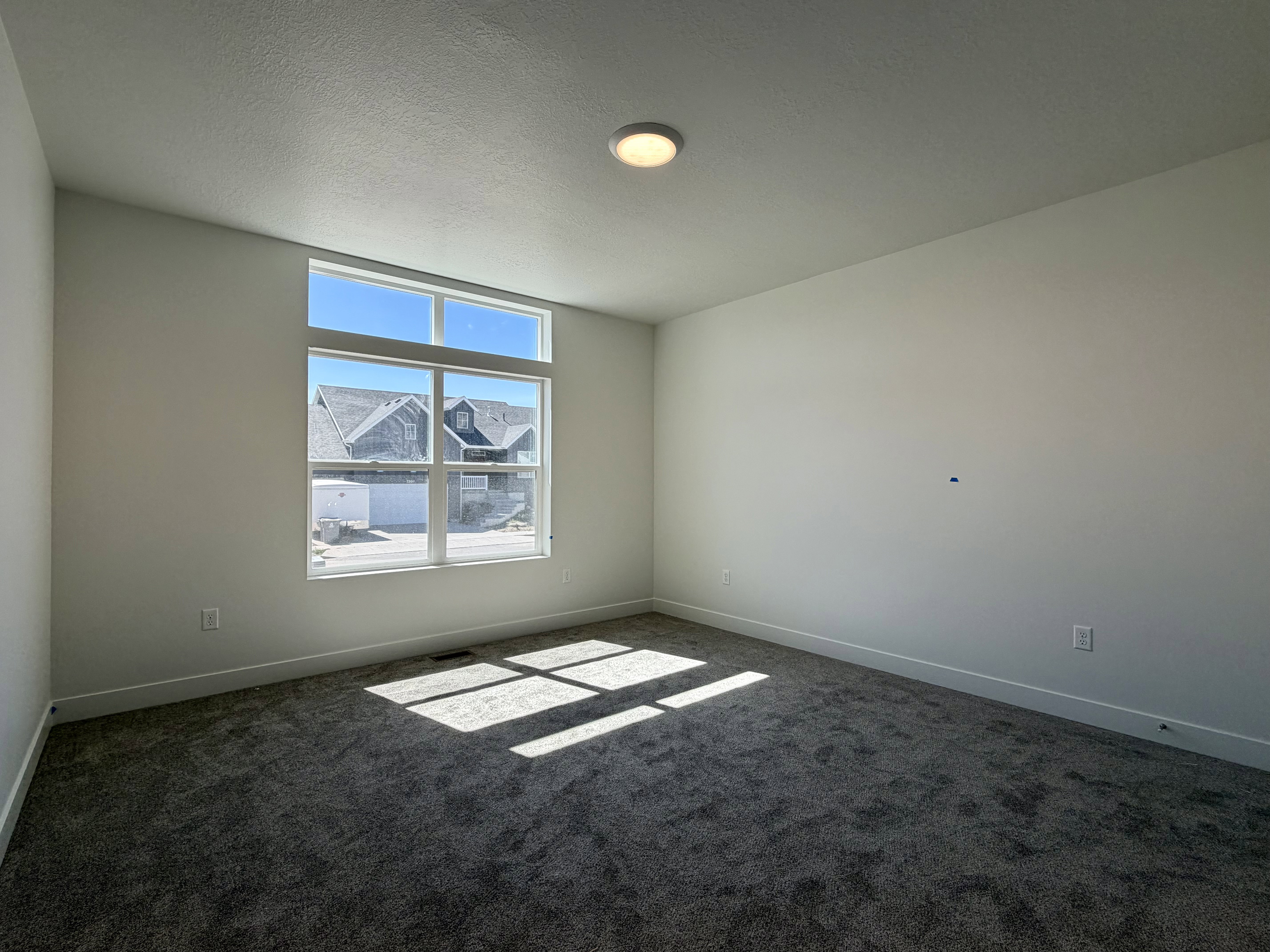 Spacious room featuring a large window with transom, neutral wall color, contemporary ceiling light fixture, and dark gray carpeting