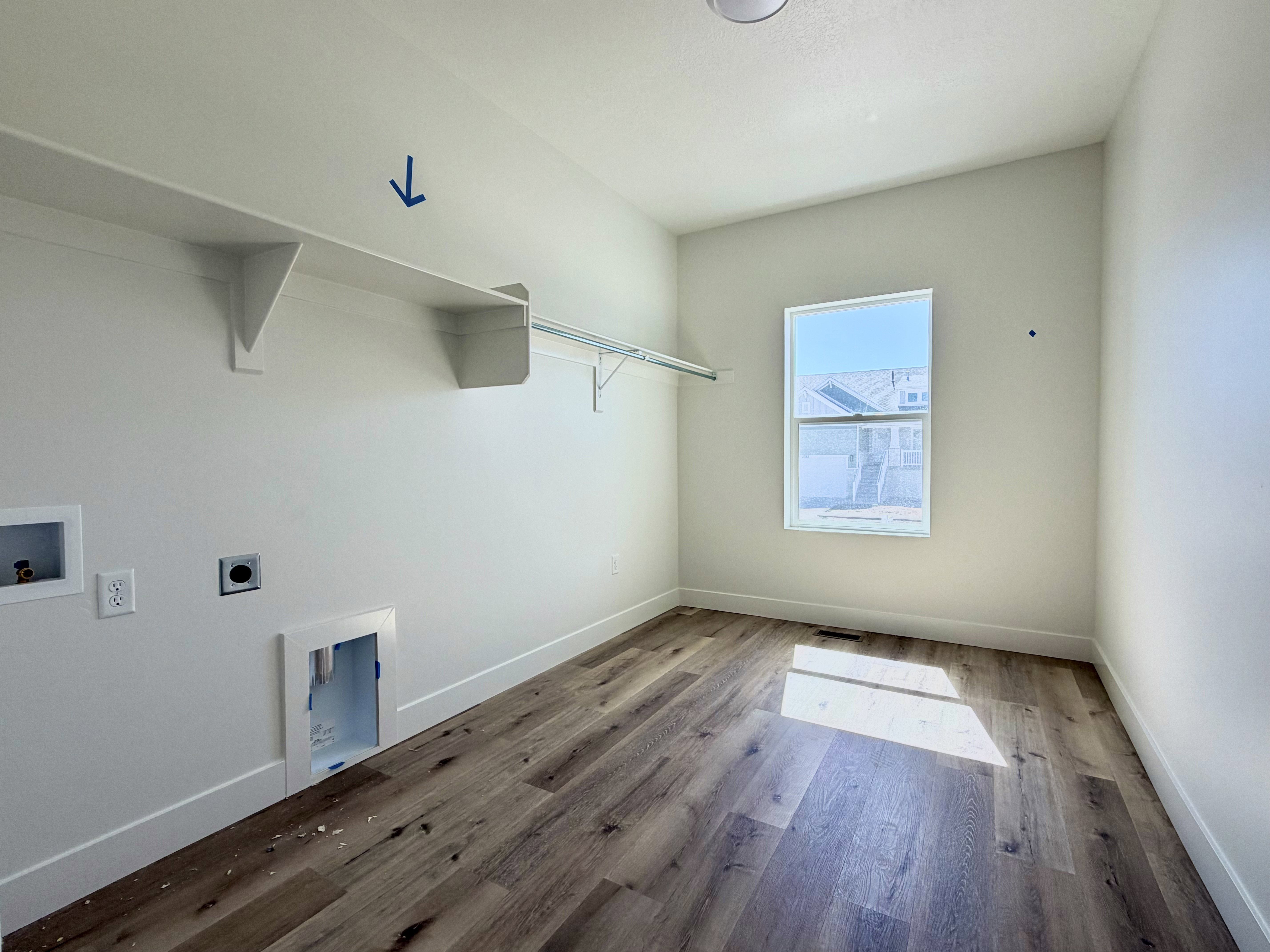 Dedicated laundry space featuring wood-finish flooring, a single window, built-in shelving, and a hanging rod