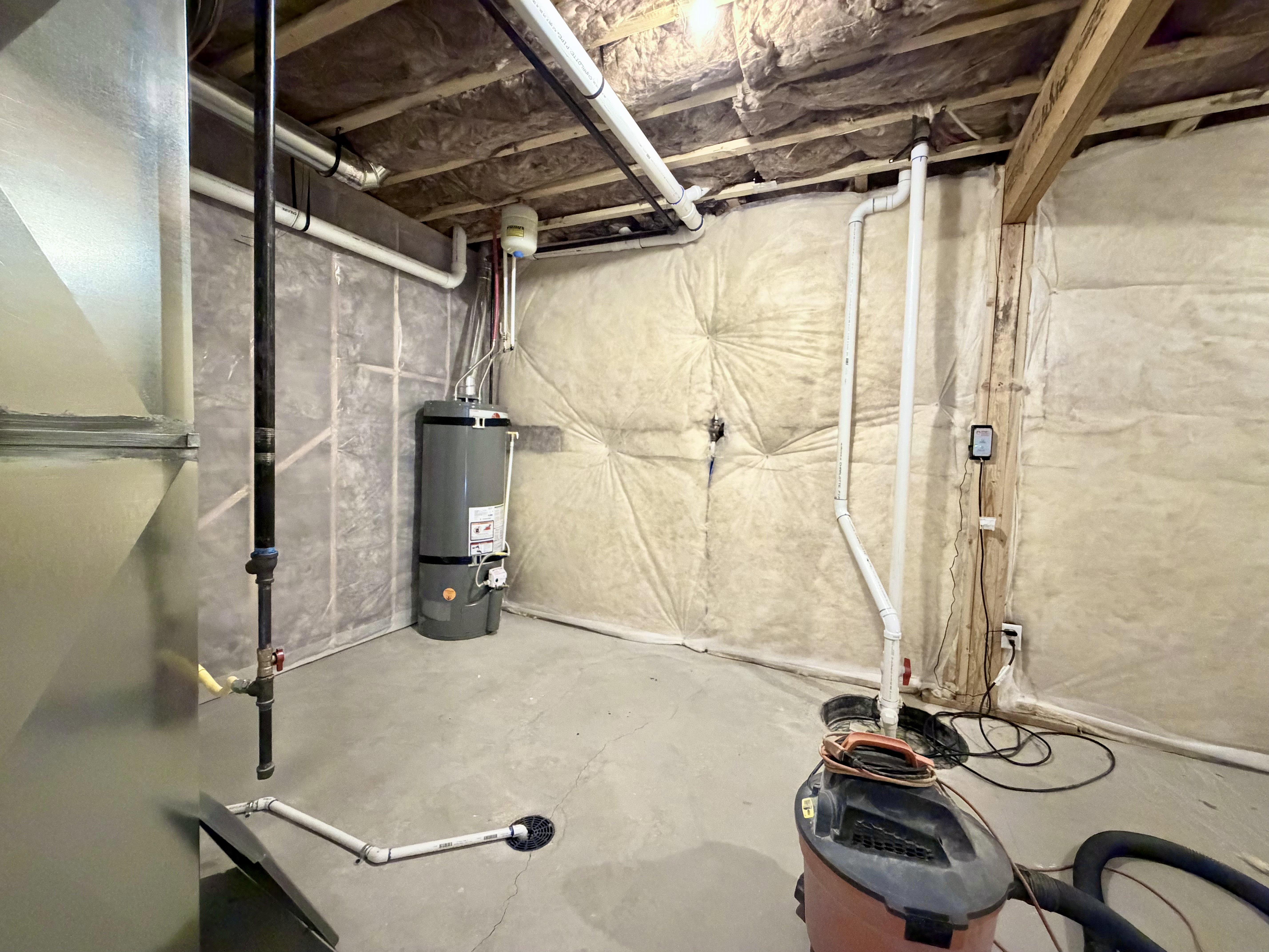 Basement utility area featuring a water heater, exposed ductwork, pipework, and insulated walls