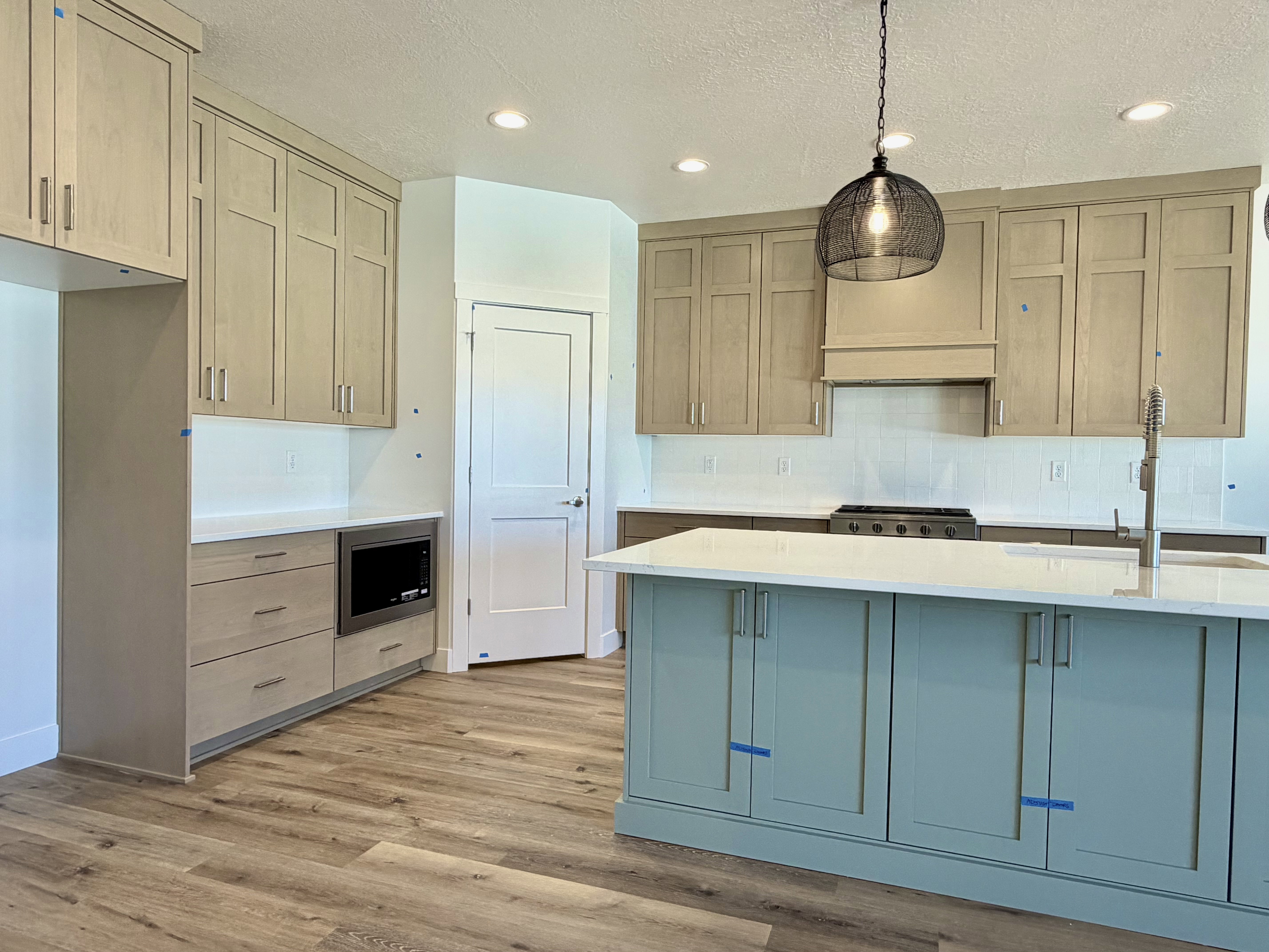 Modern kitchen featuring a light wood-finish flooring, a two-toned cabinetry scheme with a prominent light blue island, white countertops, and a white subway tile backsplash