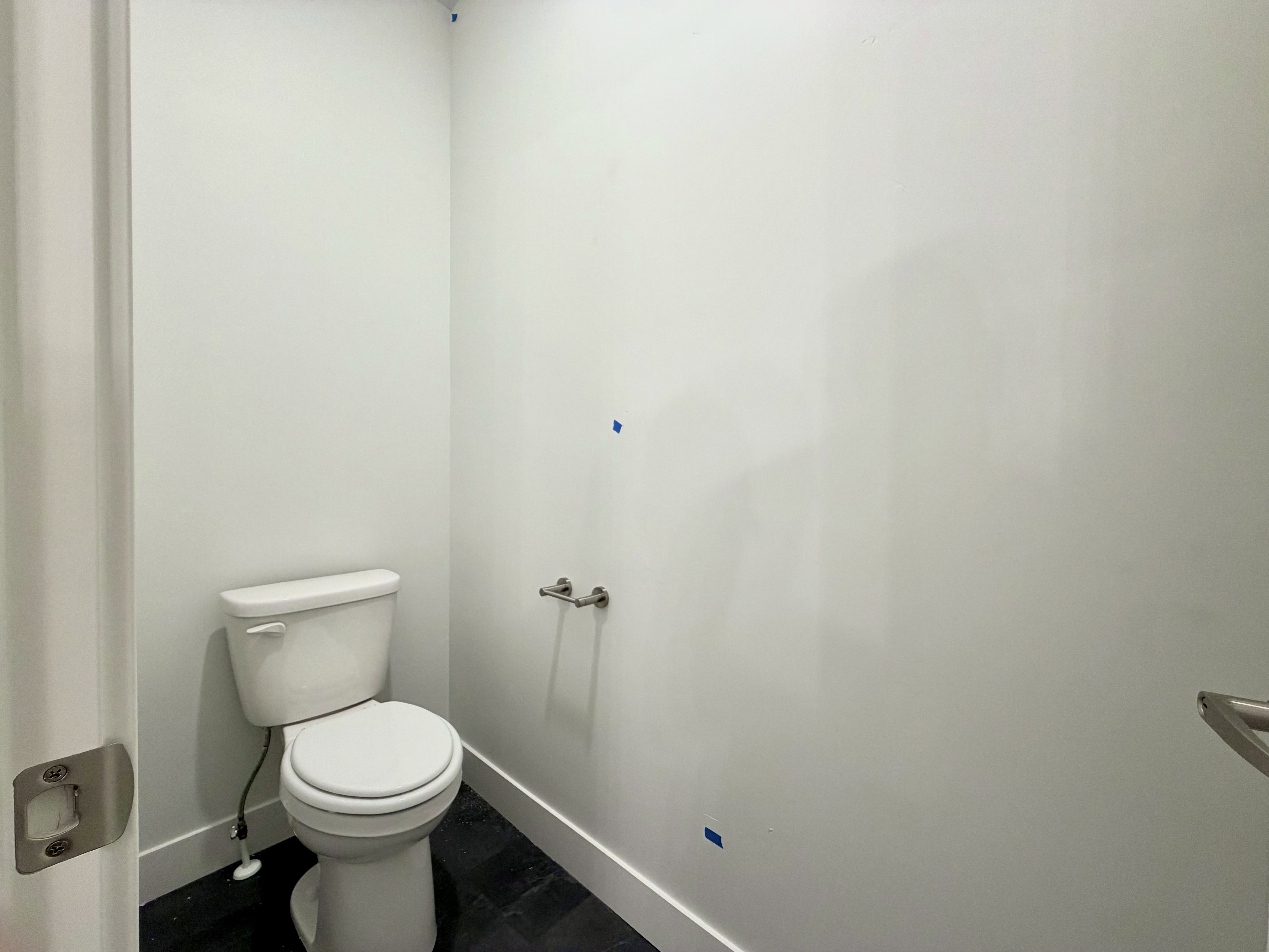 Bathroom featuring a modern white toilet, dark tile flooring, white walls, white trim, and a chrome toilet paper holder