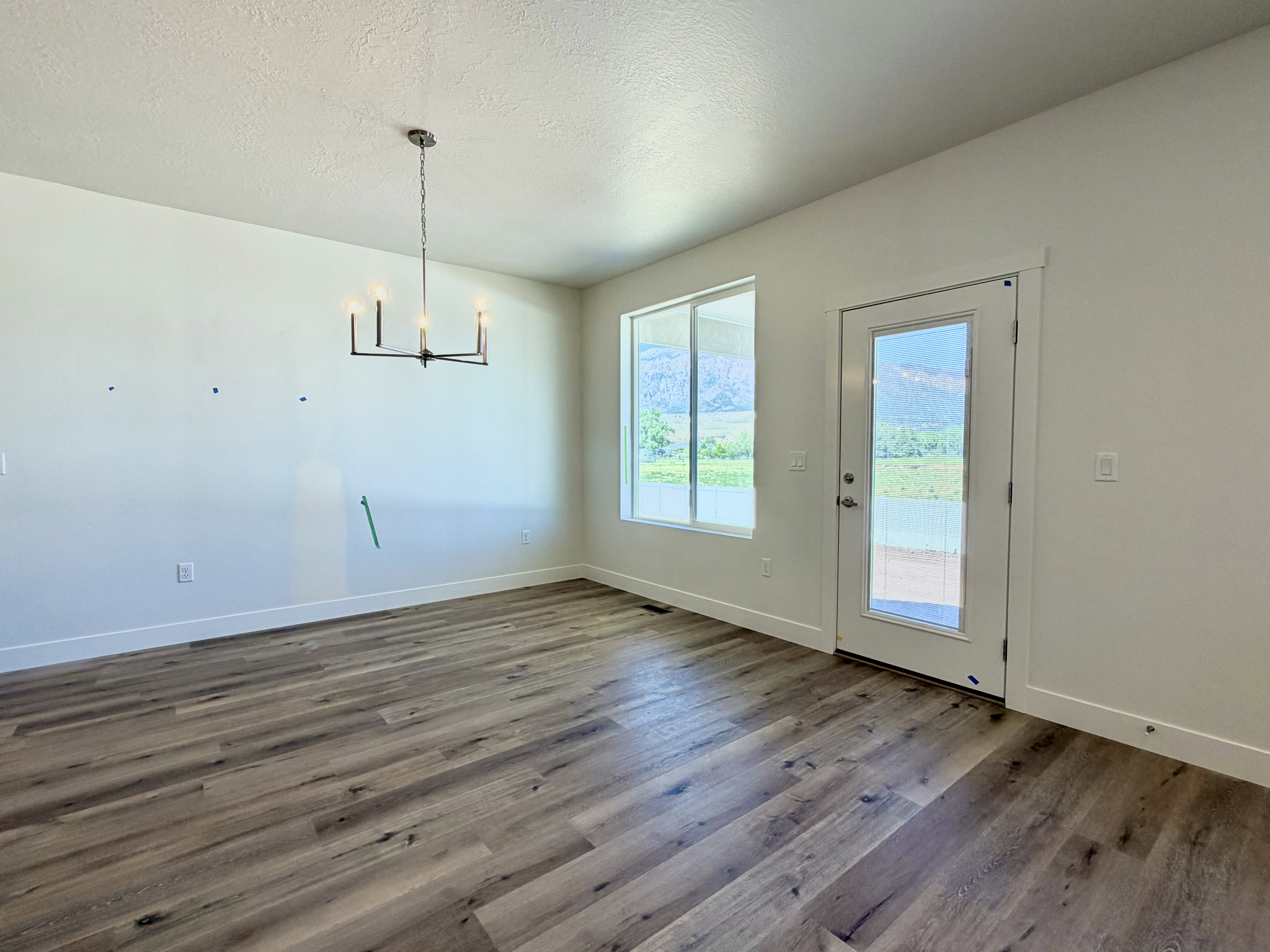 Spacious room featuring wood-finish flooring, white walls, and a modern chandelier