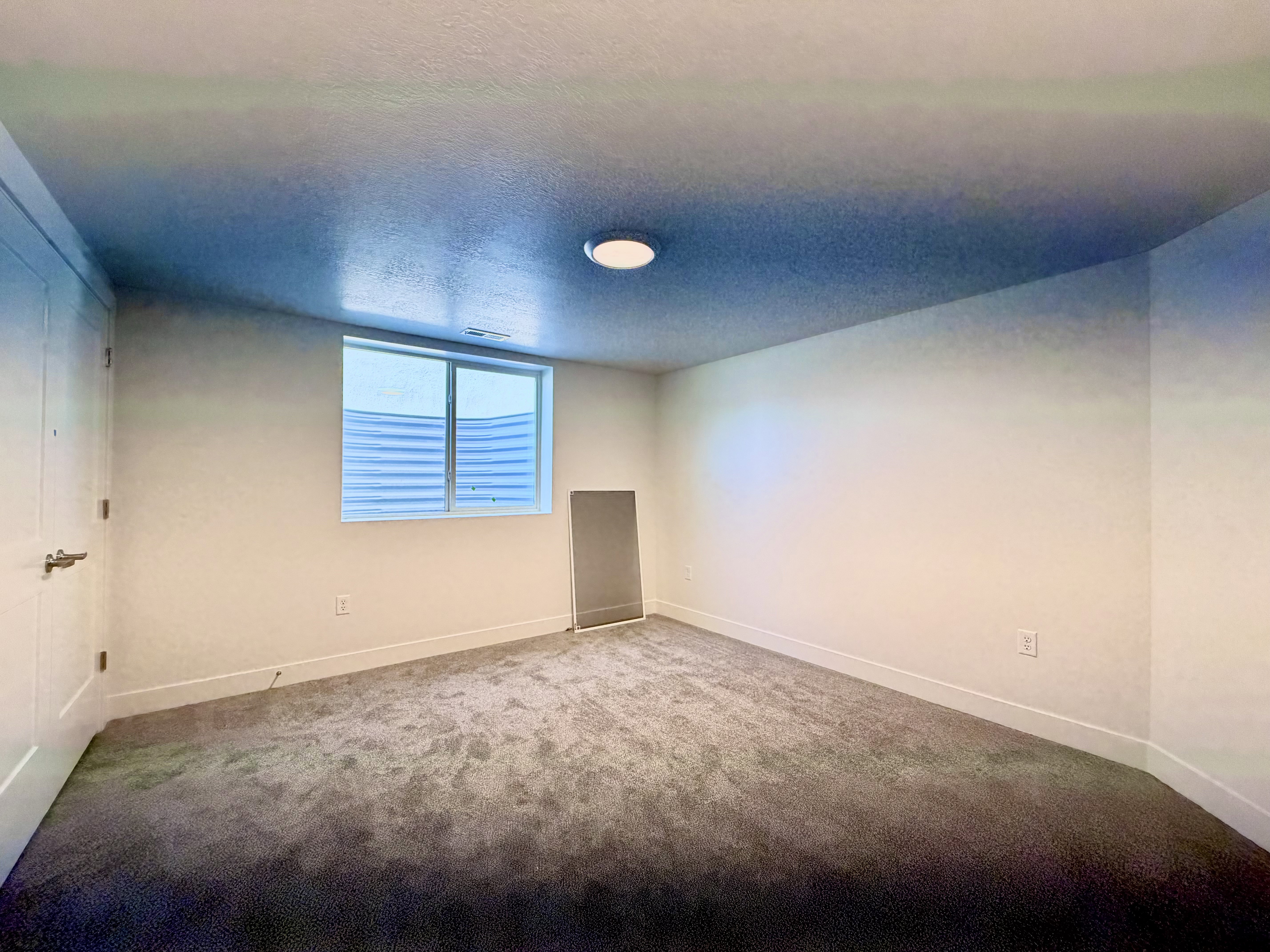 Carpeted room featuring a white door with brushed nickel hardware, a flush mount ceiling light, a window with horizontal blinds, and white baseboards