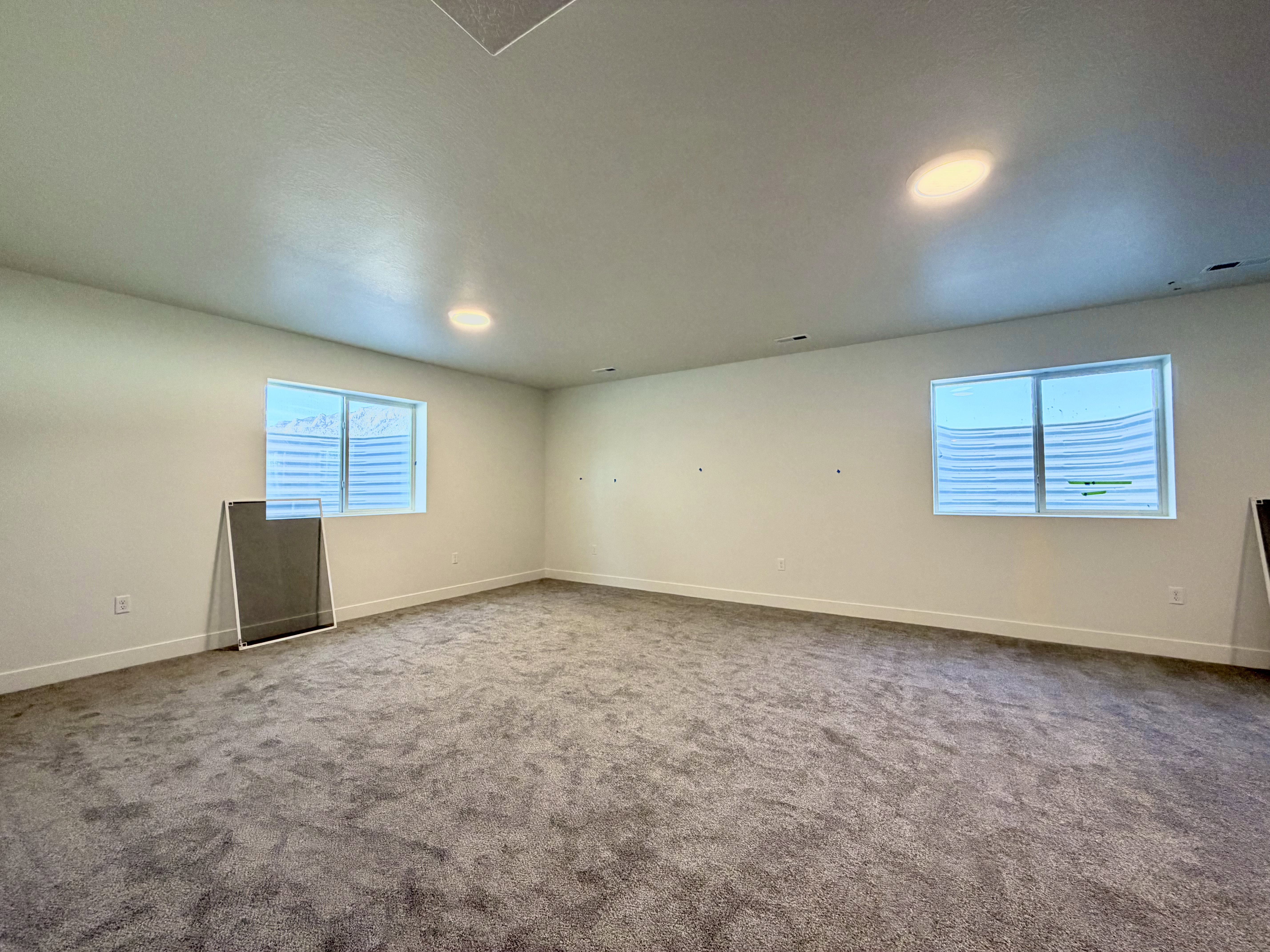 Spacious room featuring gray carpet, light-colored walls, and two egress windows