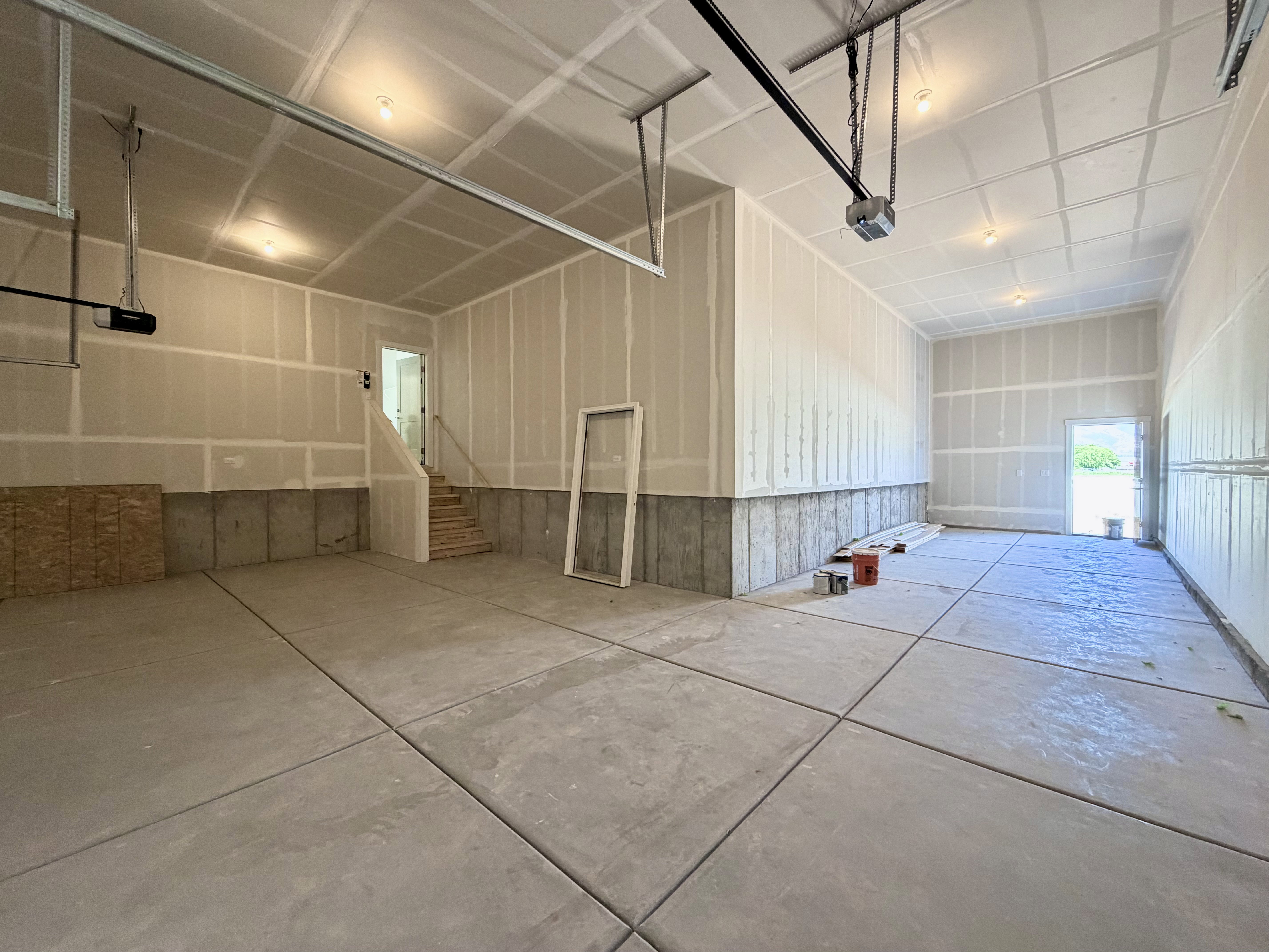 Spacious garage with concrete flooring, drywall-finished walls, built-in staircase, and integrated ceiling lighting