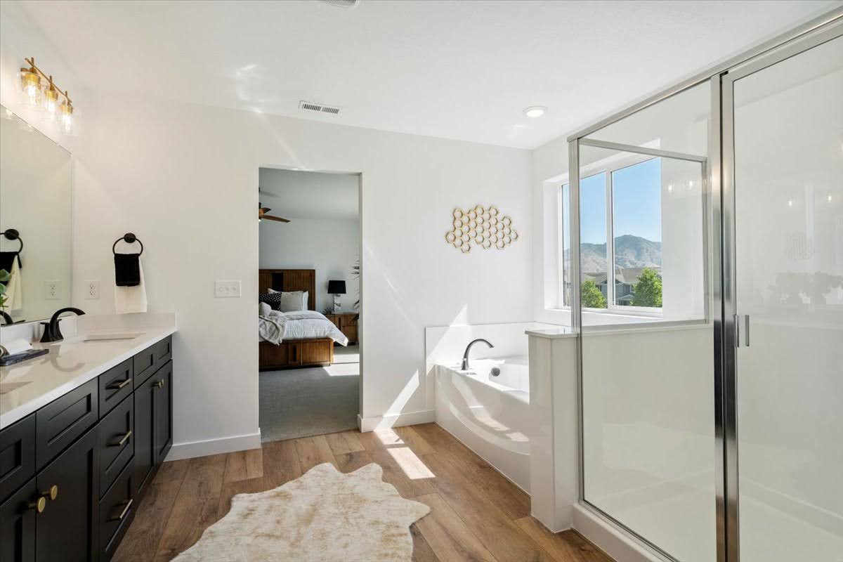 Bathroom featuring a dual vanity with dark cabinetry, integrated soaking tub, separate glass-enclosed shower, wood-finish flooring, and a window with mountain scenery