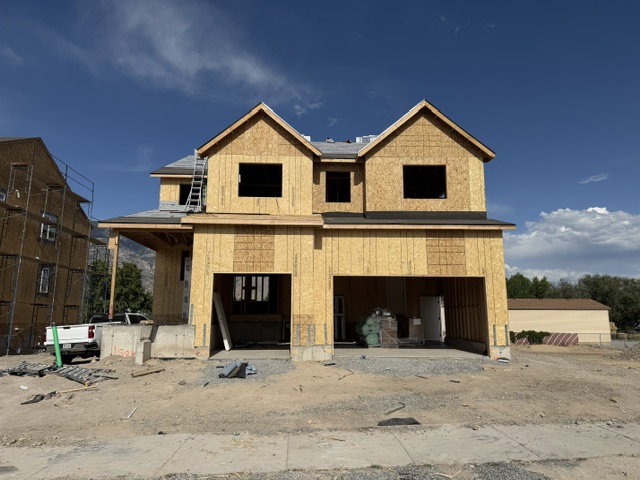 Two-story home under construction featuring a two-car garage opening, two prominent gables, a covered front porch, and a partially framed upper level
