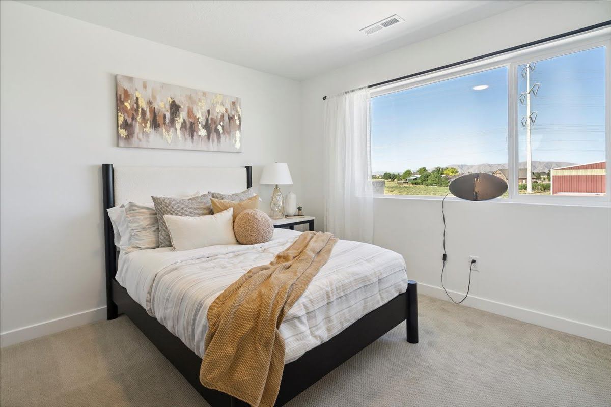 Bright bedroom featuring a large picture window, light-colored carpeting, white walls, and a recessed ceiling vent