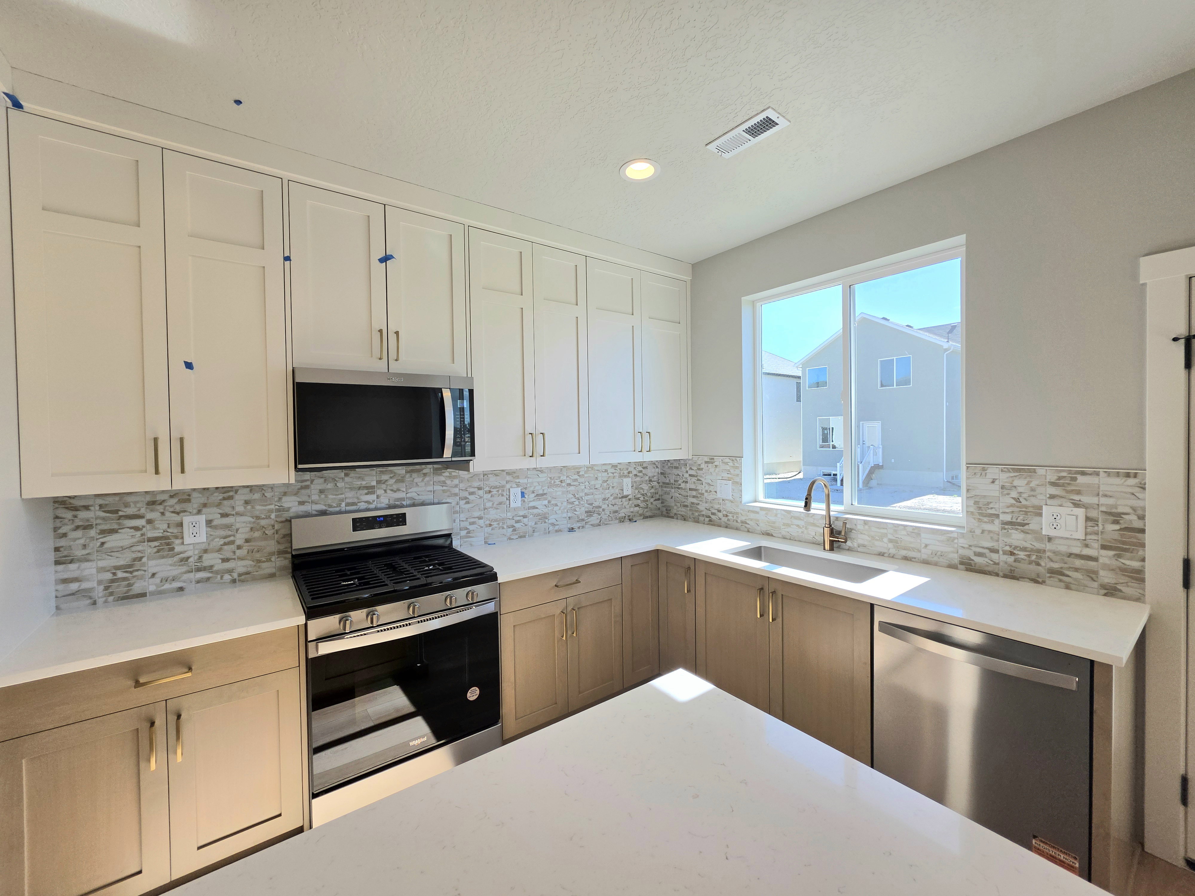 Modern kitchen featuring two-tone cabinetry, quartz countertops, and a full tile backsplash