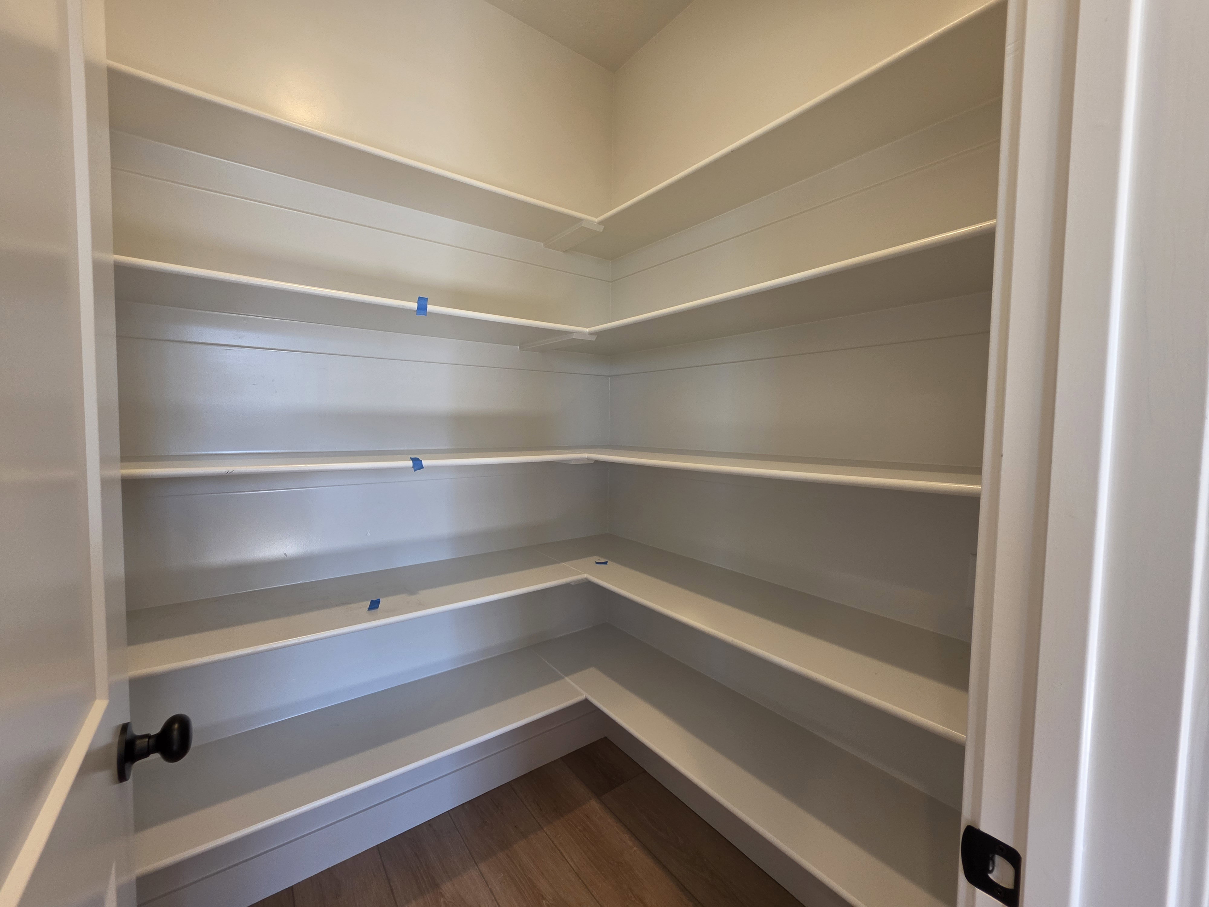 Walk-in pantry featuring extensive white shelving, L-shaped configuration, and wood-finish flooring