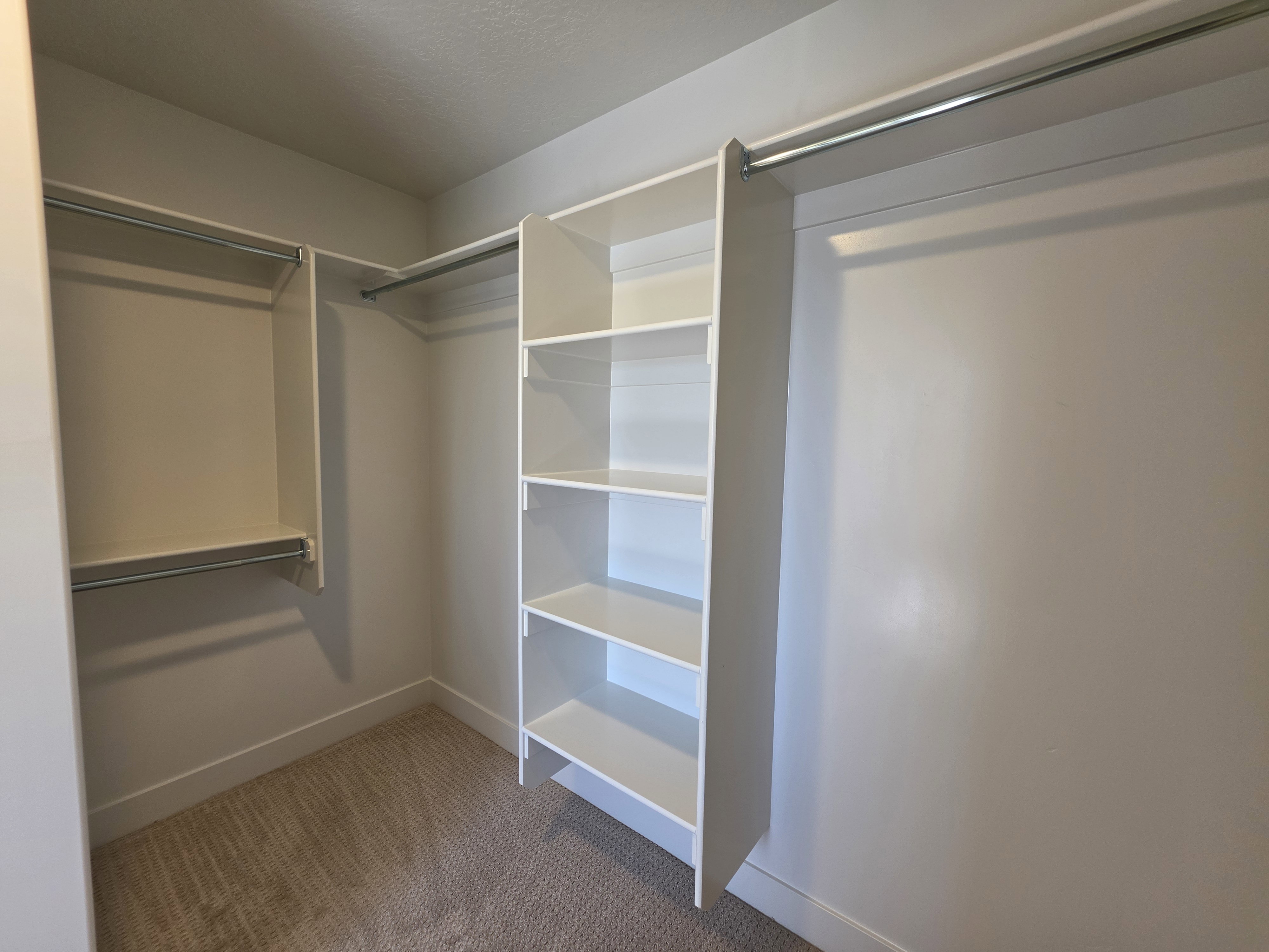 Closet featuring white built-in shelving, chrome hanging rods, and light-toned carpet flooring