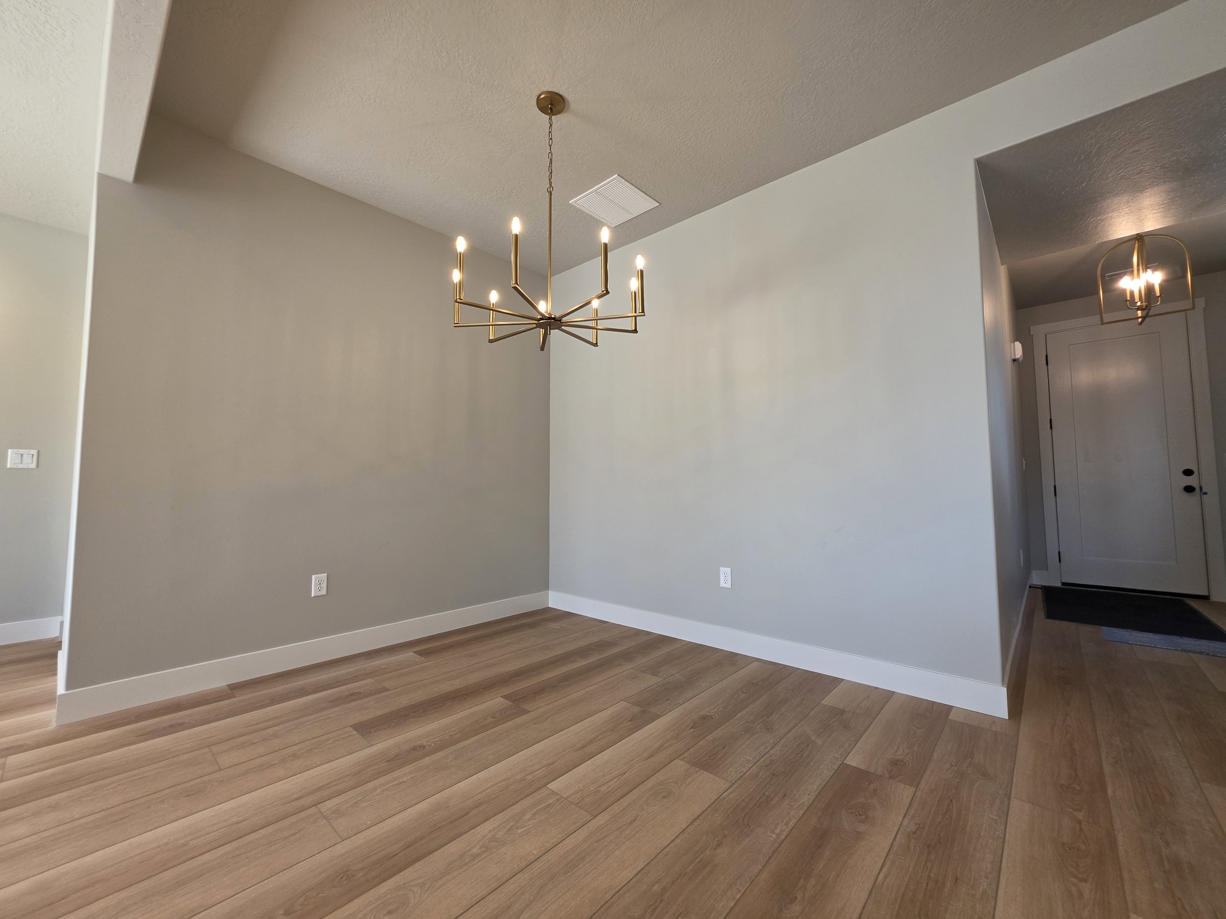 Spacious room featuring wood-finish flooring, a modern brass chandelier, and neutral wall tones