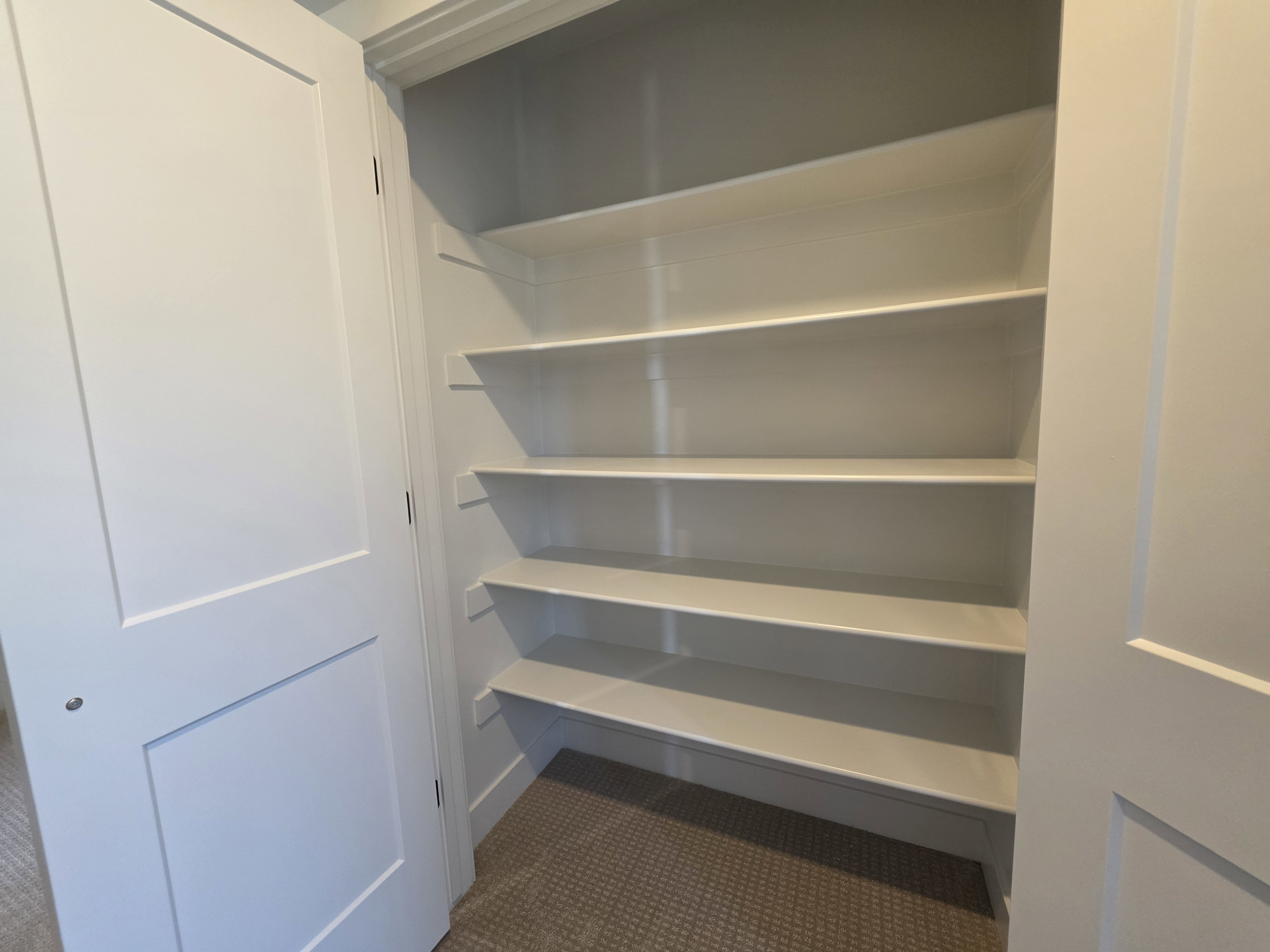 Built-in shelving unit featuring multiple white shelves, a neutral carpeted floor, and white paneled bifold doors