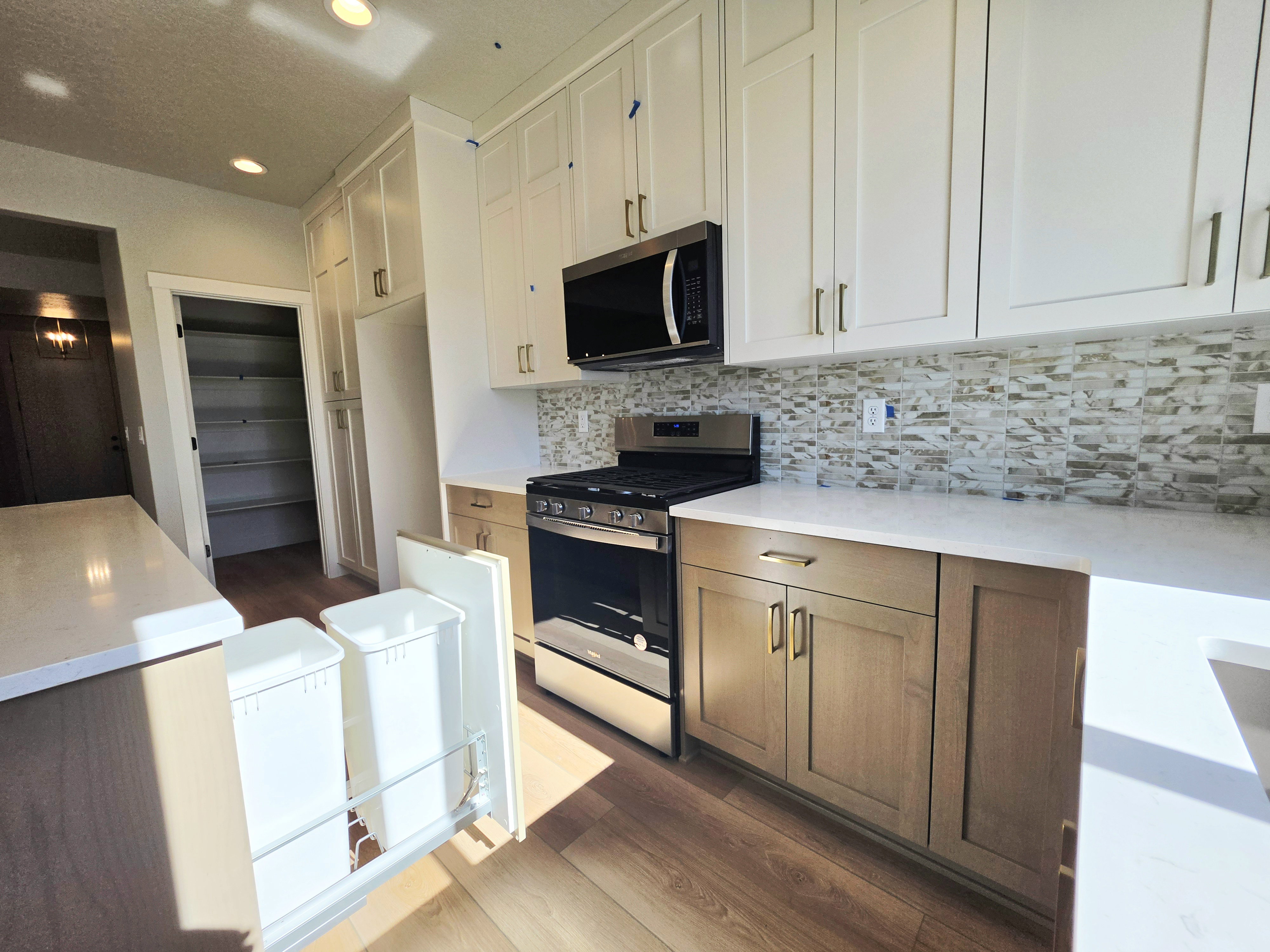 Modern kitchen featuring two-tone cabinetry with gold-tone hardware, stainless steel appliances, a mosaic tile backsplash, and light-toned countertops