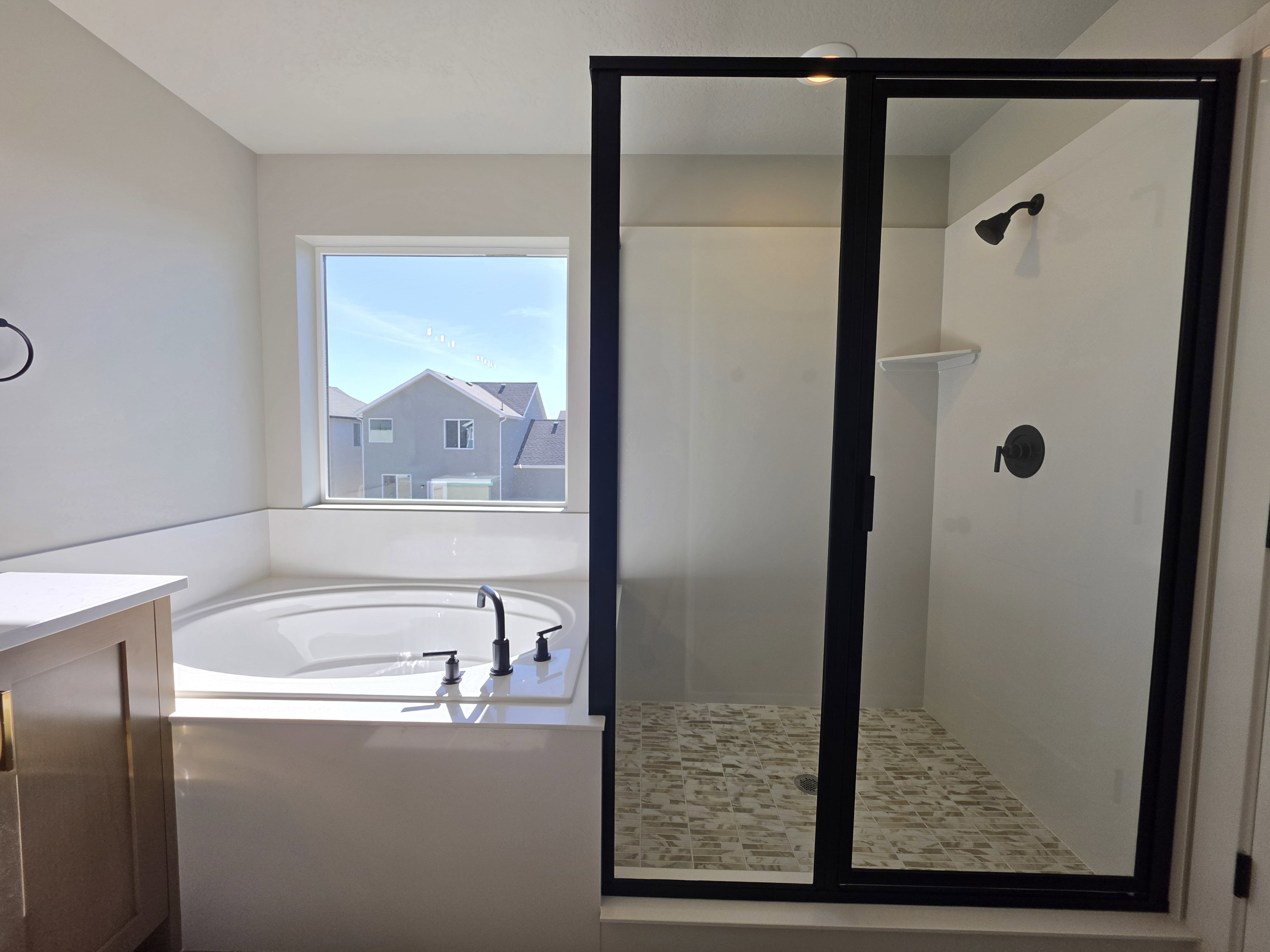 Bathroom featuring a built-in soaking tub with black fixtures, a walk-in shower with black-framed glass enclosure, and a mosaic tile shower floor