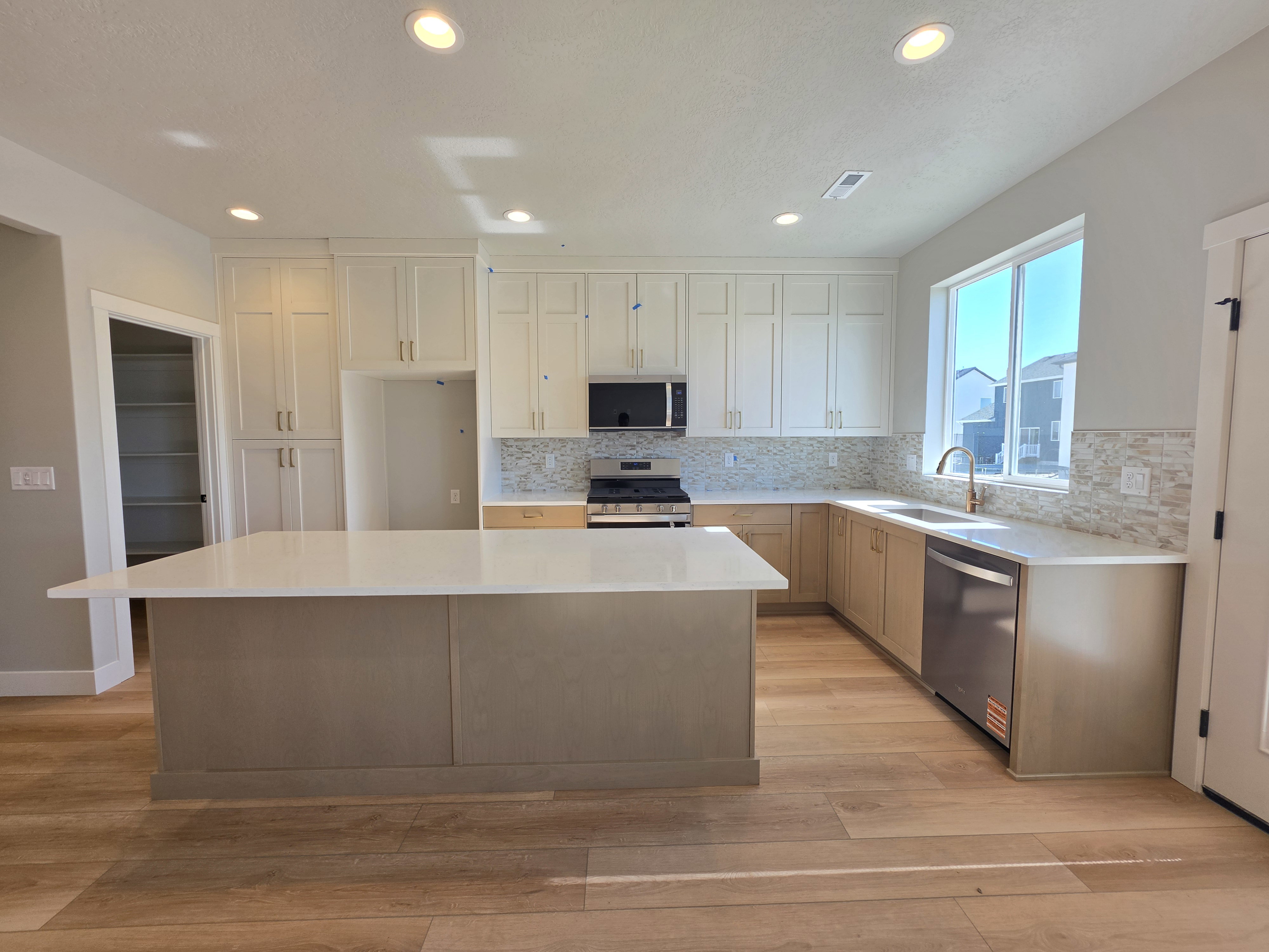 Kitchen featuring a large island with a light-toned countertop, wood-finish flooring, white upper cabinetry, natural wood-finish lower cabinetry, and stainless steel appliances