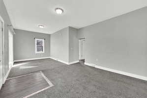 Spacious room with light gray walls, dark gray carpeting, and white baseboards