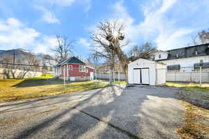 Paved driveway leading to a detached white storage shed with double doors