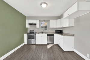 Kitchen featuring wood-finish flooring, white cabinetry, stainless steel appliances, and a window above the sink