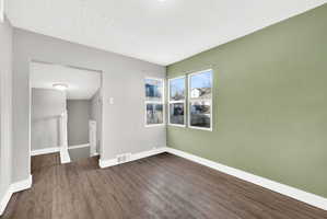 Living area featuring wood-finish flooring, light green accent wall, three pane windows, and an arched doorway leading to a staircase