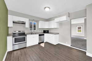 Kitchen featuring white cabinetry, stainless steel appliances, speckled countertops, and wood-finish flooring