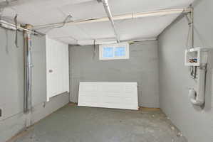Concrete basement walls with a single window and exposed utility piping