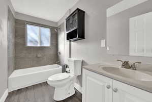 Full bathroom featuring a white bathtub with subway tile surround, a single window, a white vanity with integrated sink, and wood-finish flooring